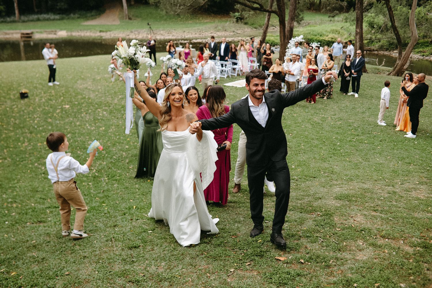 Outdoor wedding ceremony setup with white chairs arranged on a grassy lawn under tall trees.