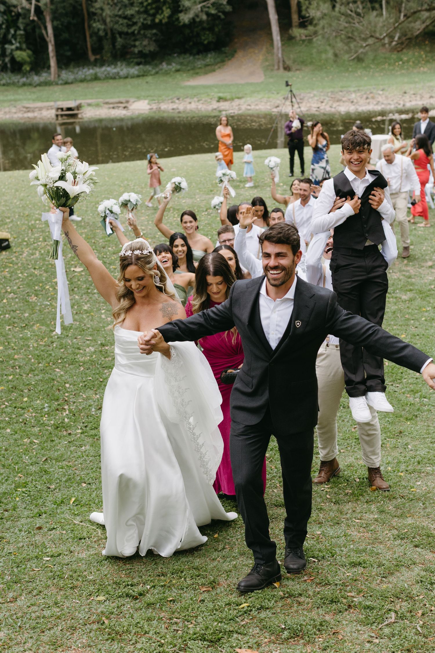 Wedding party celebrates joyfully on grassy lawn during outdoor reception.
