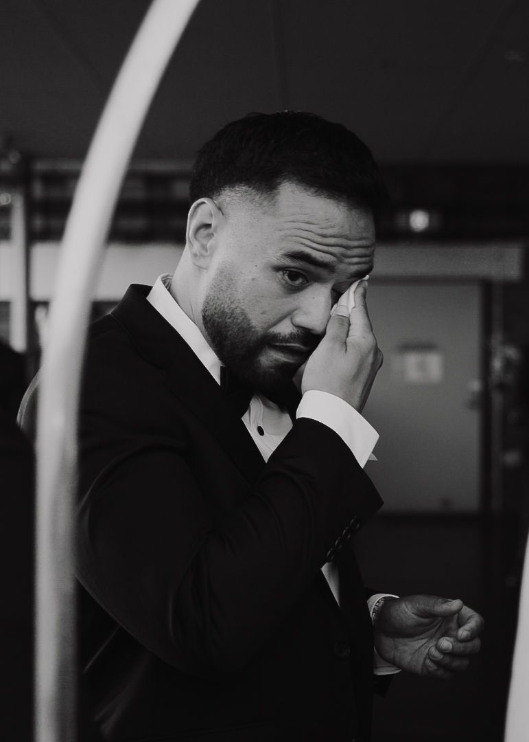 A person in a black suit smiles and gestures while looking down in a series of black and white photos.