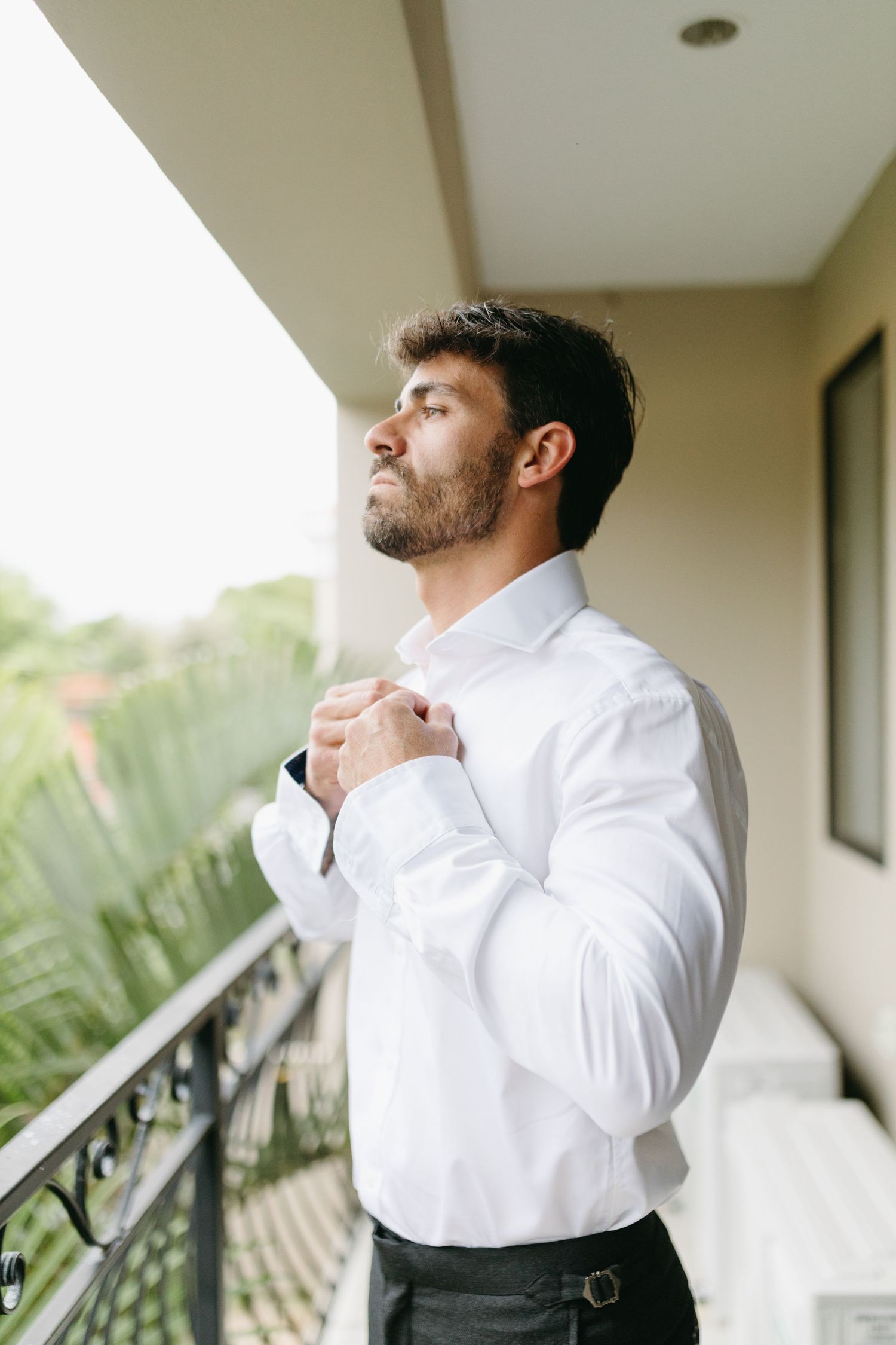 A person in a crisp white dress shirt adjusting their collar on a balcony.