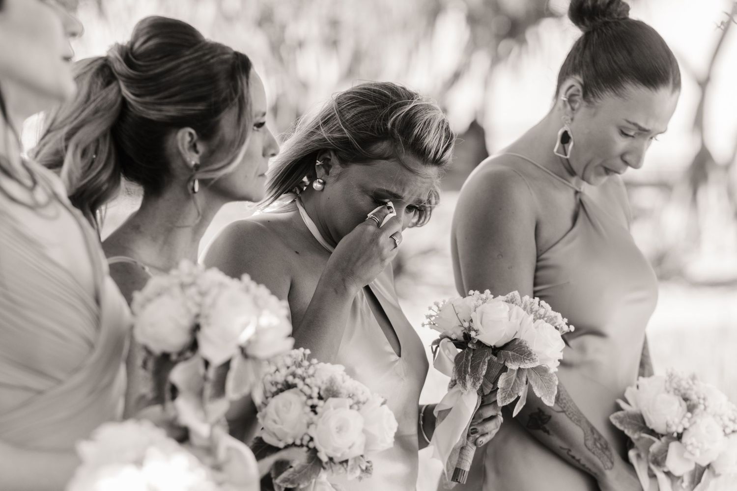 Row of bridesmaids wiping tears during emotional wedding ceremony.