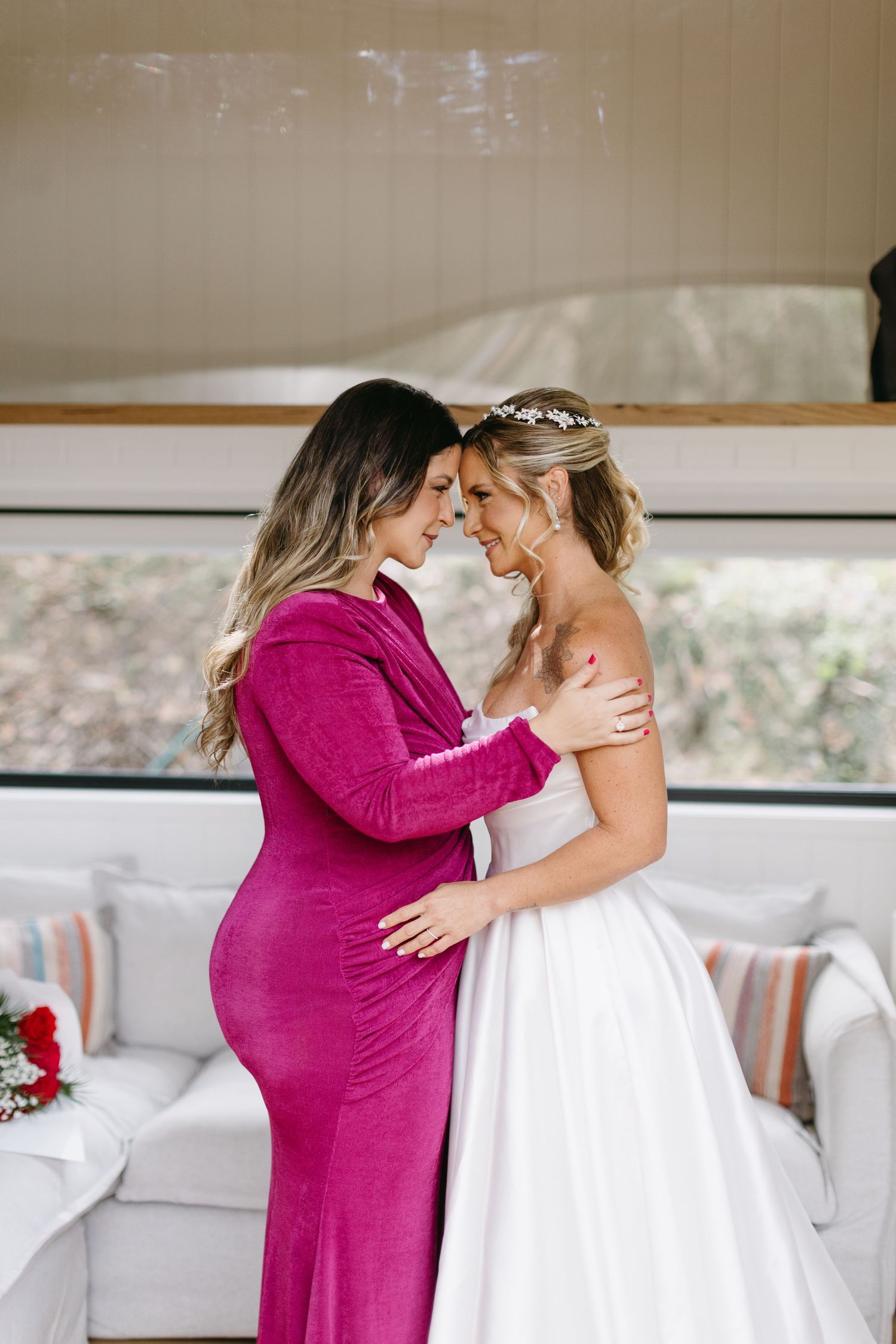 Emotional moment between bride and loved one in magenta dress during wedding preparations.