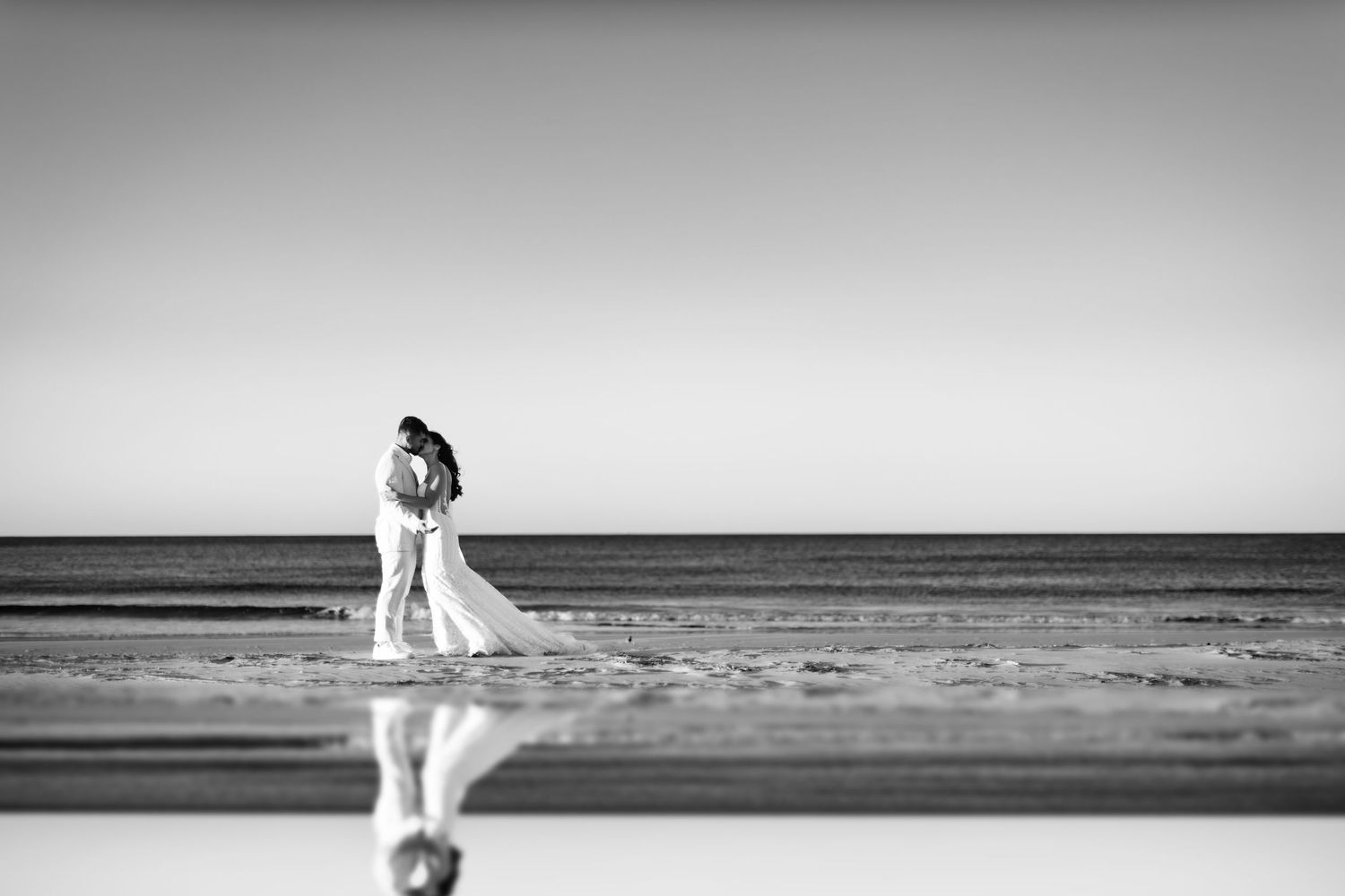 Minimalist beach wedding photos with distant figures against an ocean horizon.