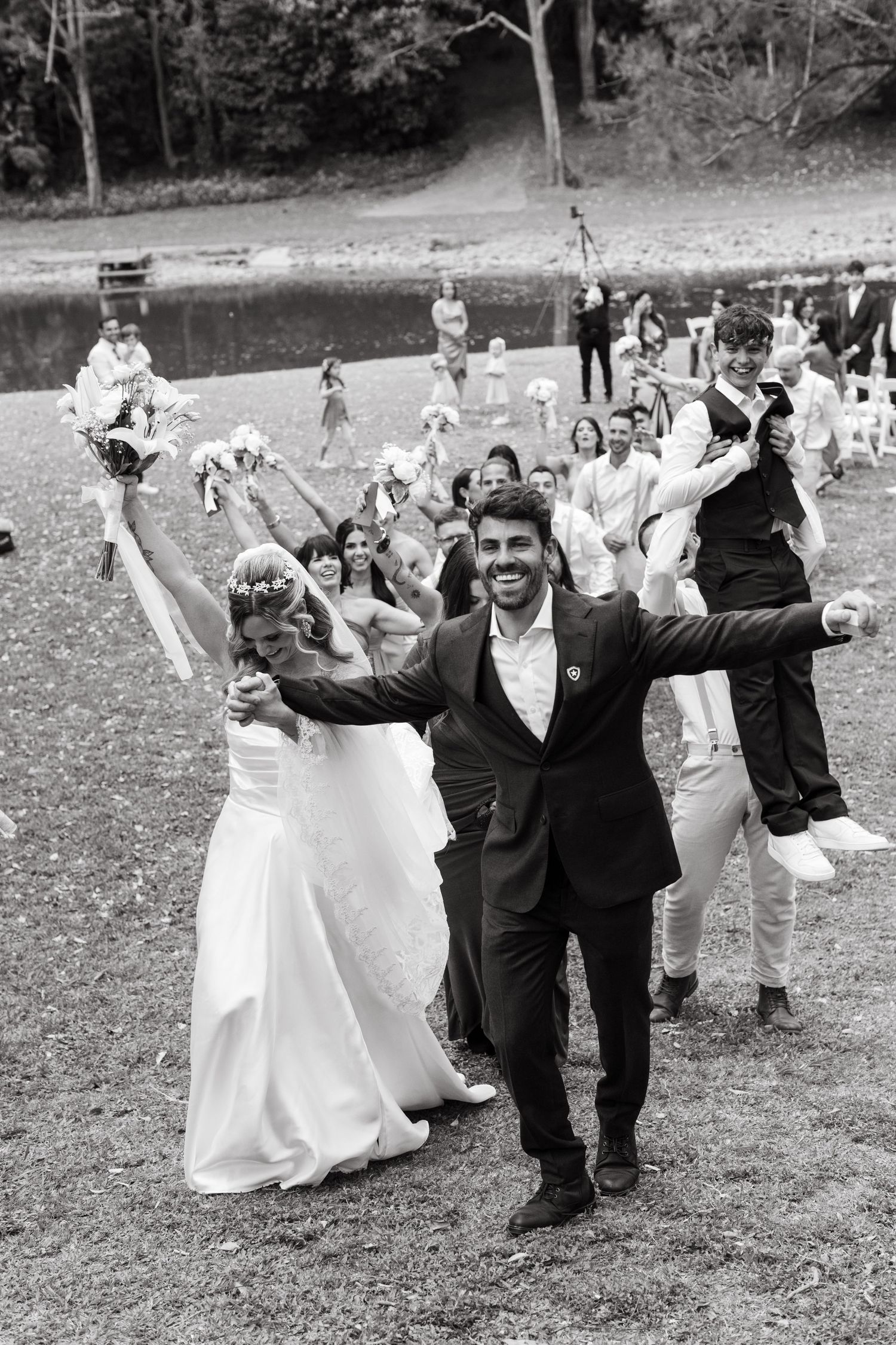 Wedding party members in formal attire performing synchronized dance moves on a grassy lawn.
