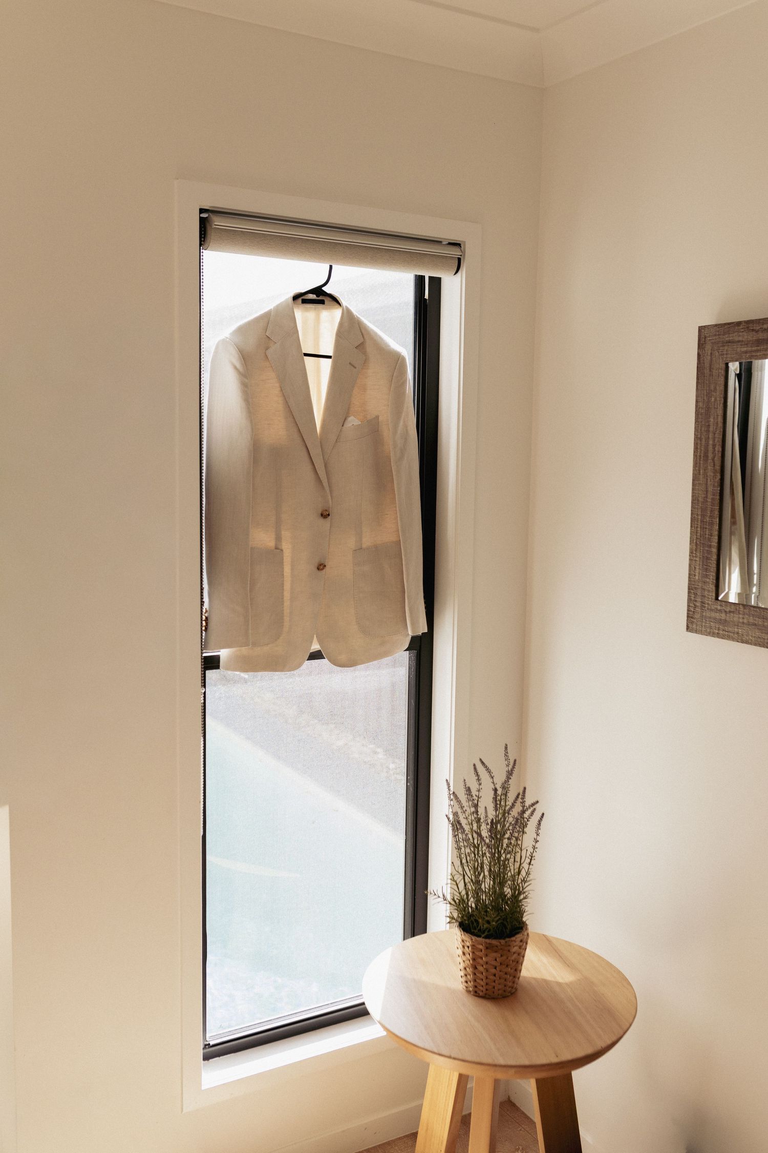 A minimalist white room with a window, displaying a beige blazer and small potted plant on a curved white surface.