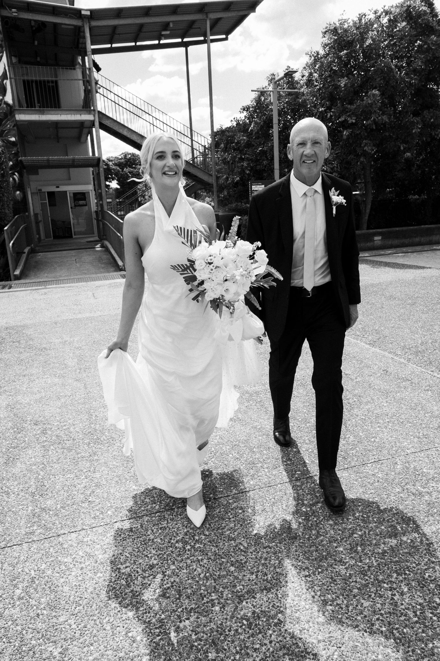 A wedding couple walking outdoors in black and white, with the bride in a flowing white dress holding a bouquet.