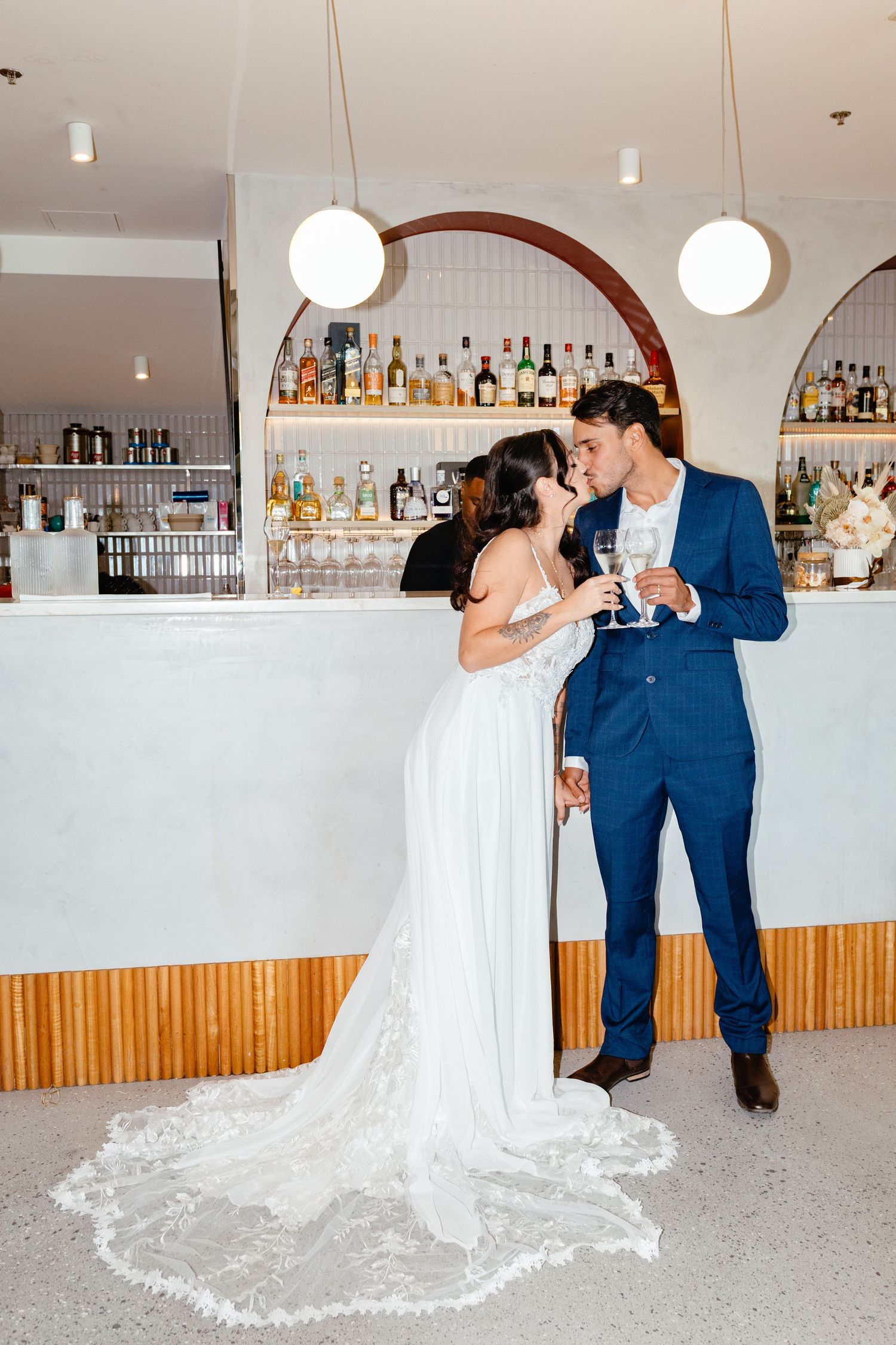 Newlyweds share romantic moments at a bar reception venue with white and wooden decor.