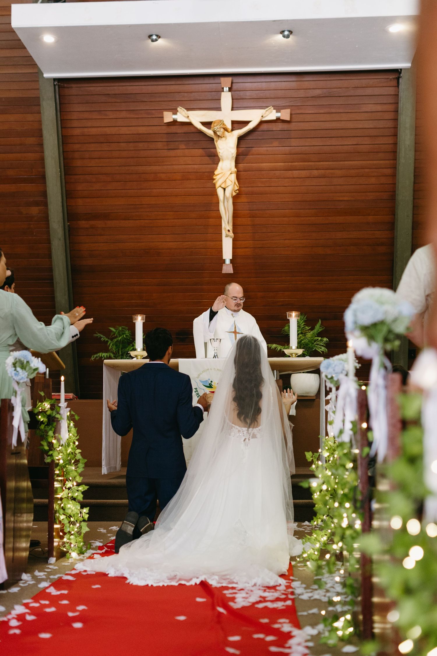 A wedding ceremony in progress at a Catholic church with decorative lights and floral arrangements.