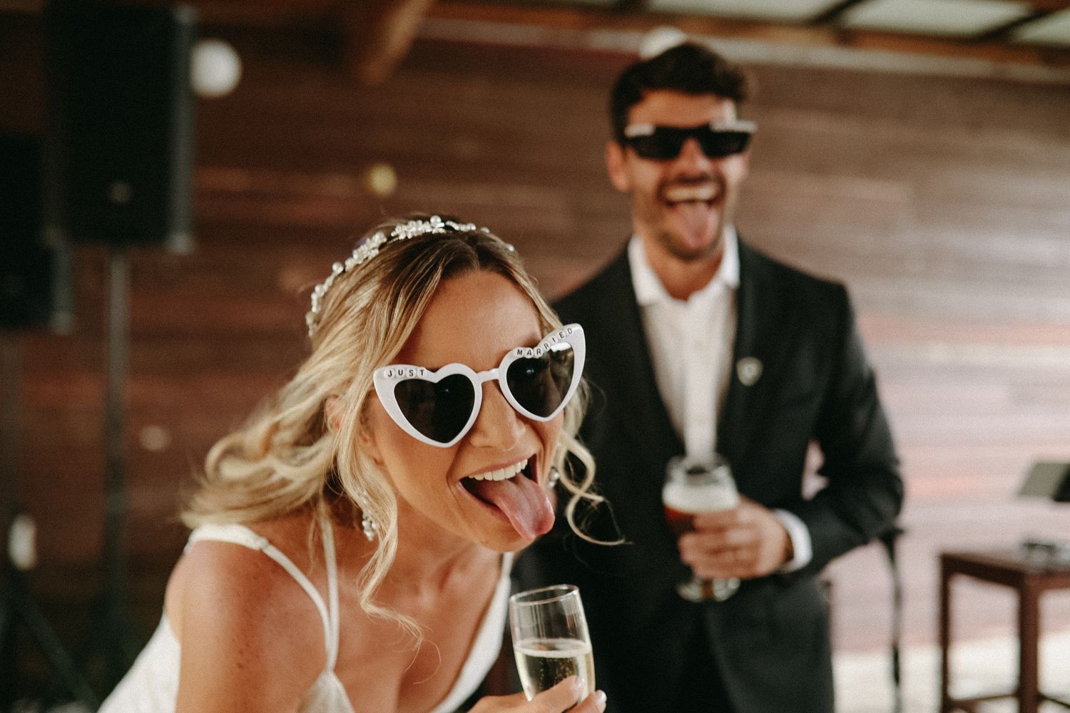Wedding party wearing sunglasses and formal attire celebrating with champagne outdoors.