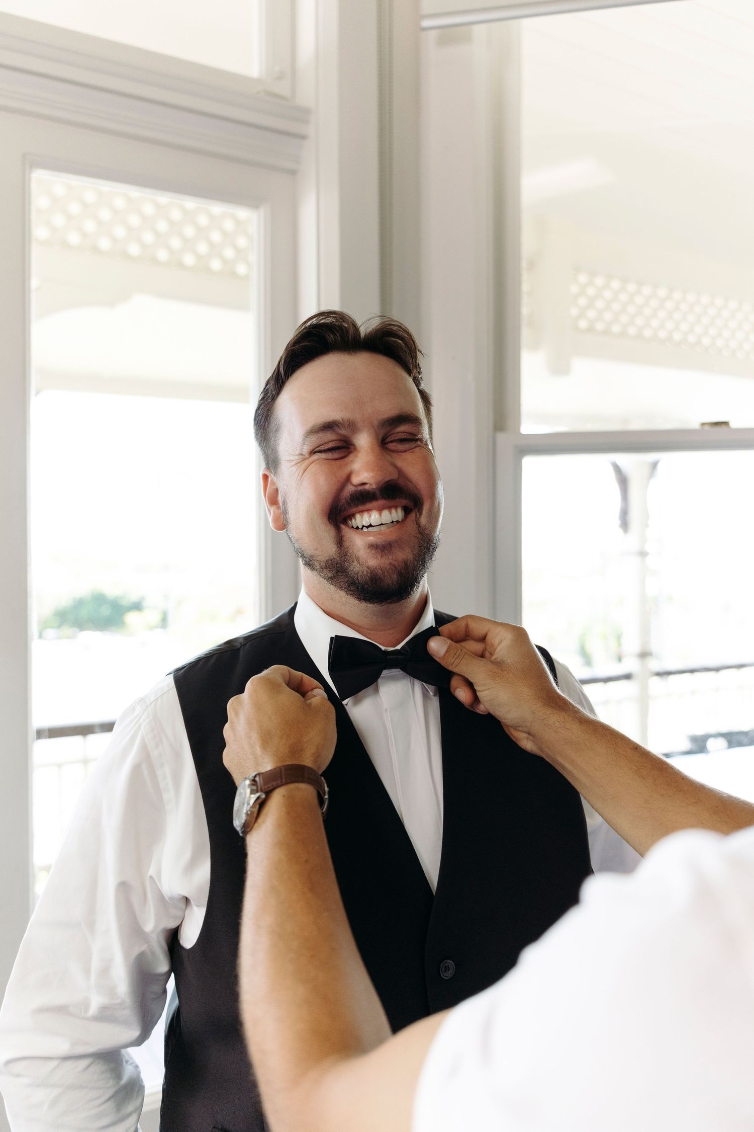 A person in a black vest and bowtie laughs heartily in a sequence of candid shots.