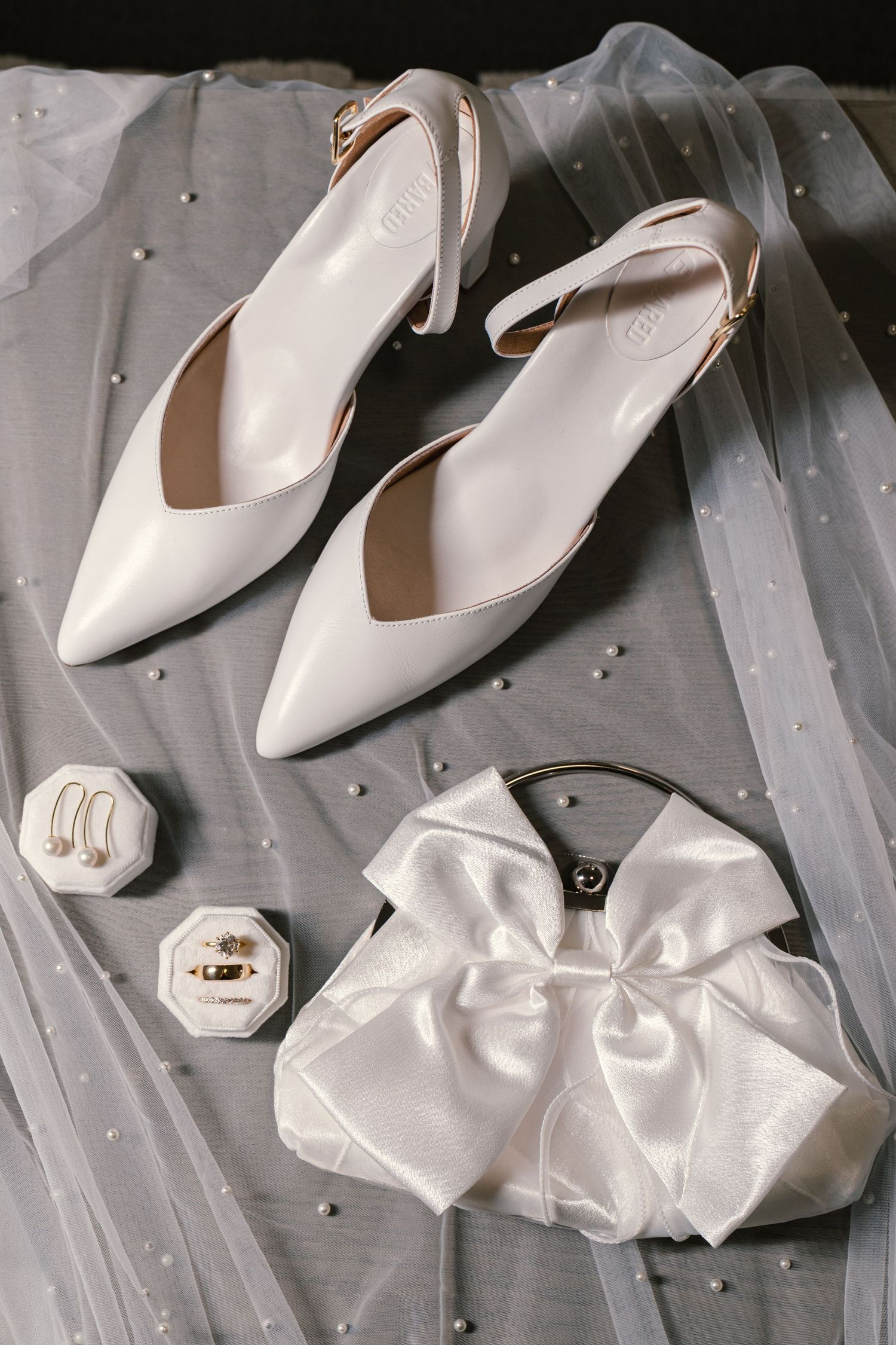 White bridal shoes and satin bow accessories arranged on a grey textured surface.