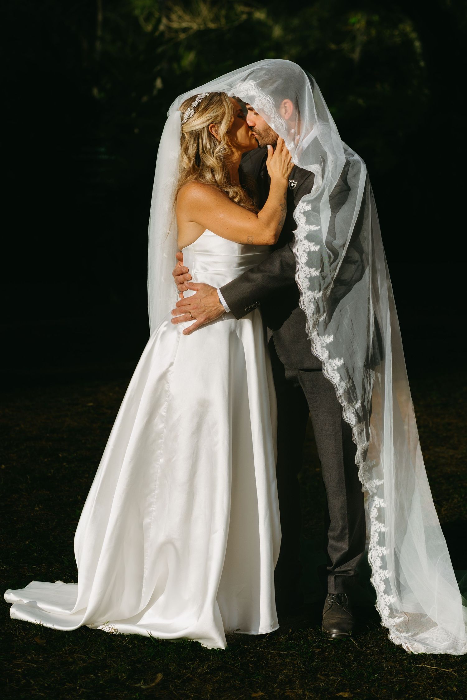 Romantic wedding couple embraces under a flowing white veil in a garden.