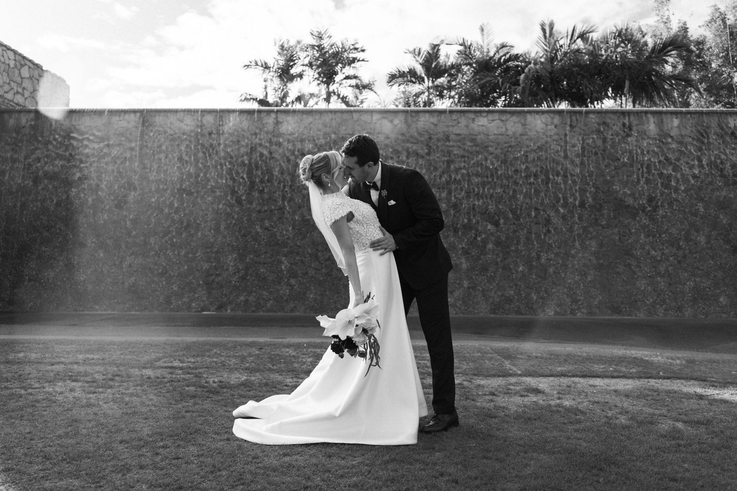 Black and white photo of a bride and groom sharing a romantic kiss in front of a waterfall wall.