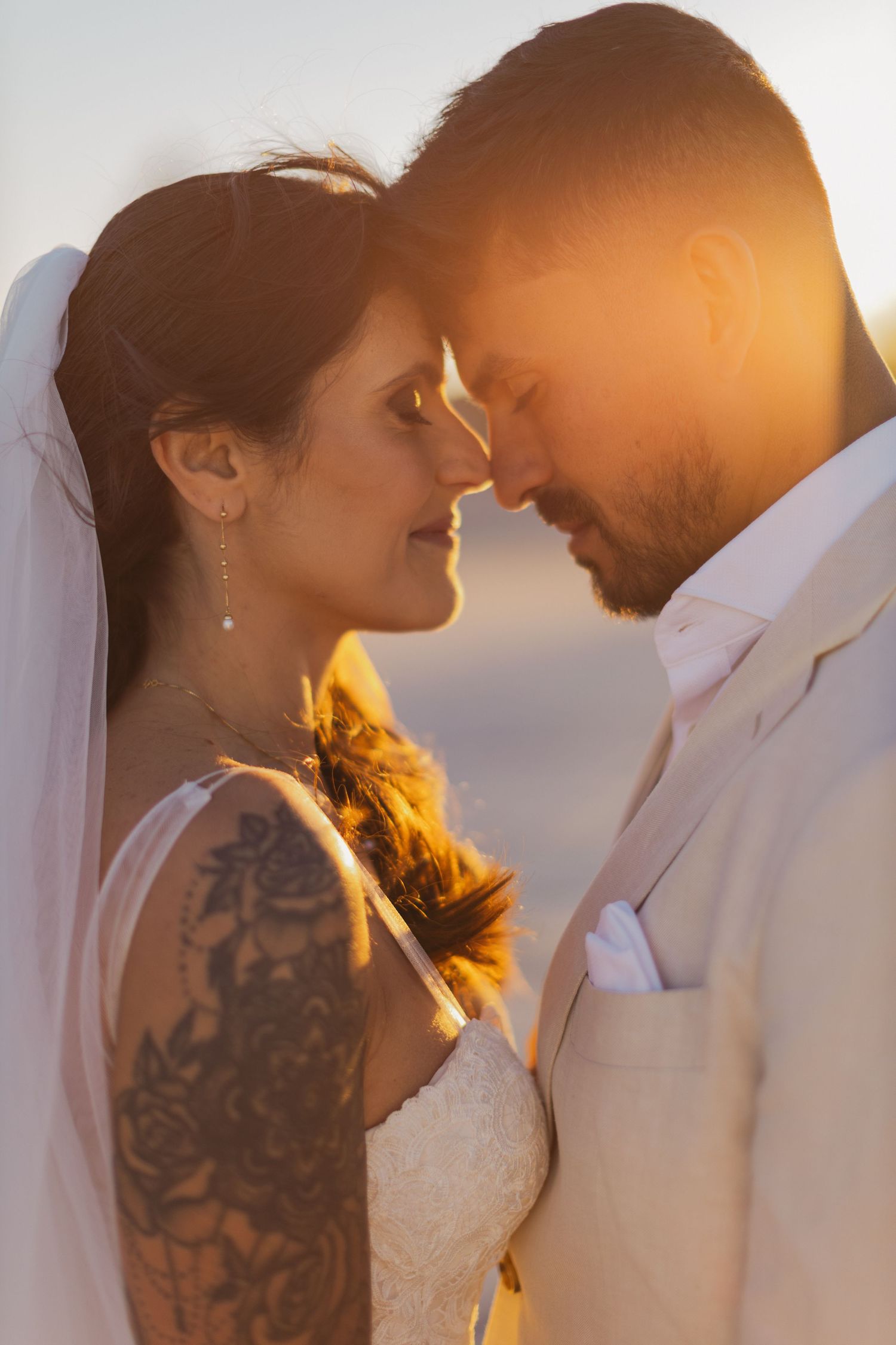 A romantic sunset wedding portrait shows a couple touching foreheads with golden light glowing behind them.