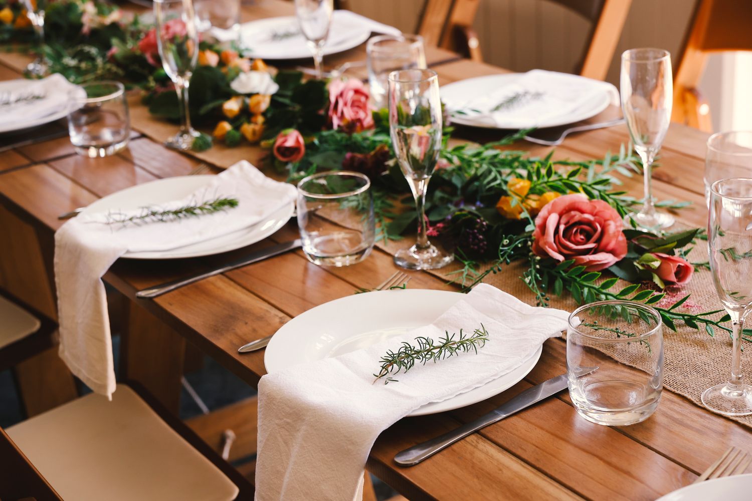 Rustic wooden tables decorated with floral centerpieces, greenery, and elegant place settings for a wedding reception.