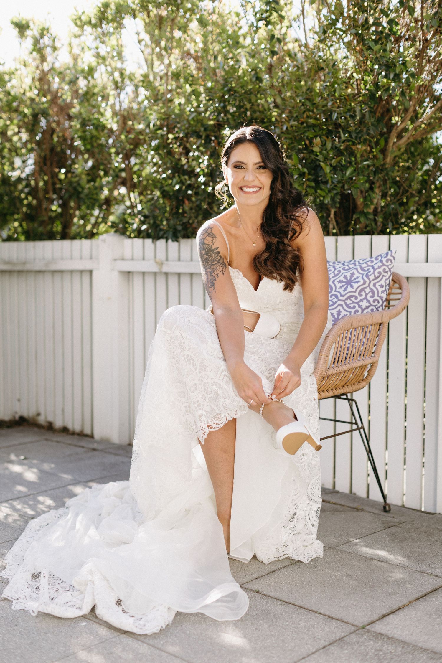White lace wedding dress with intricate details displayed on a sunny patio with white picket fence.