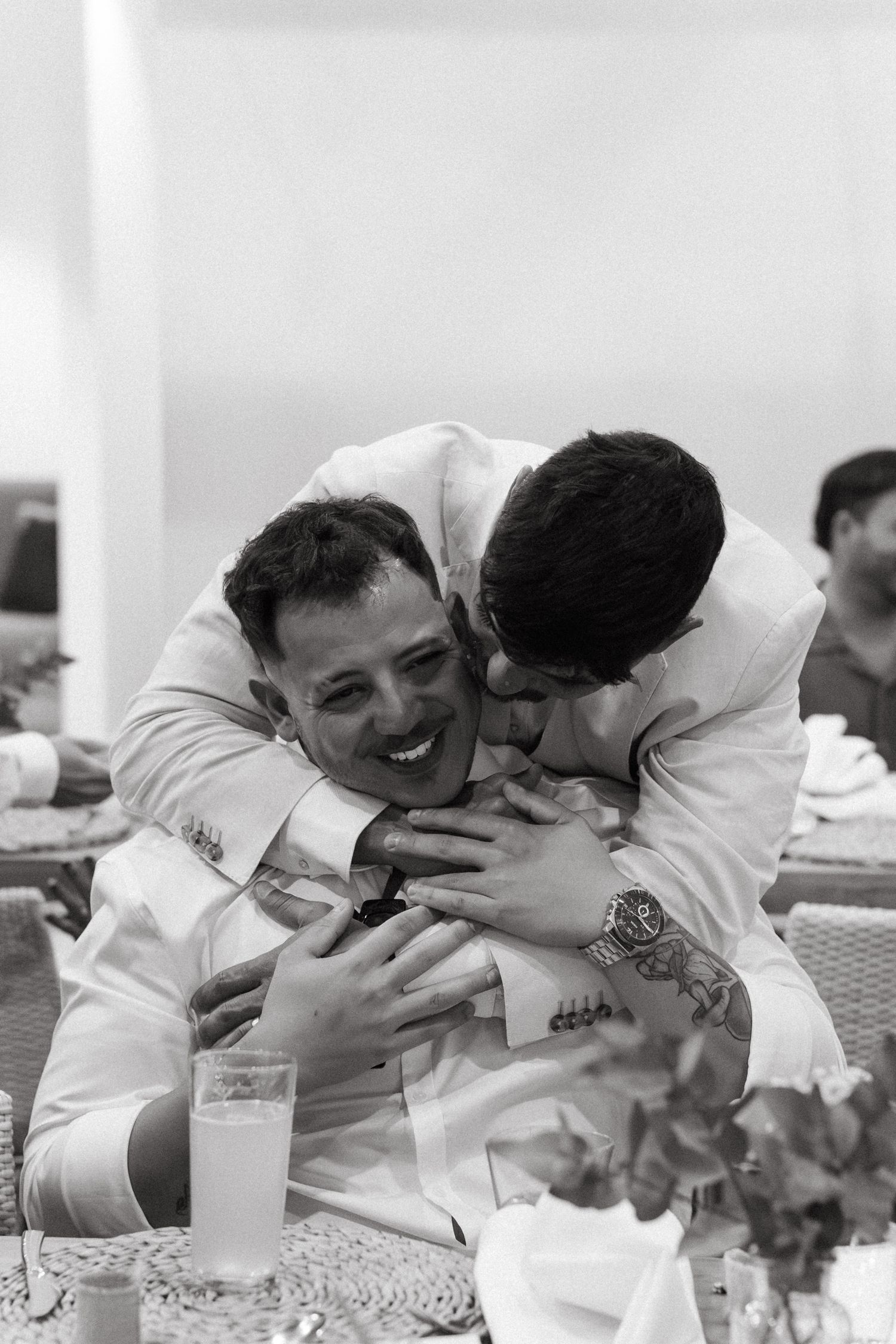 Two people in white attire embrace emotionally during a wedding celebration.
