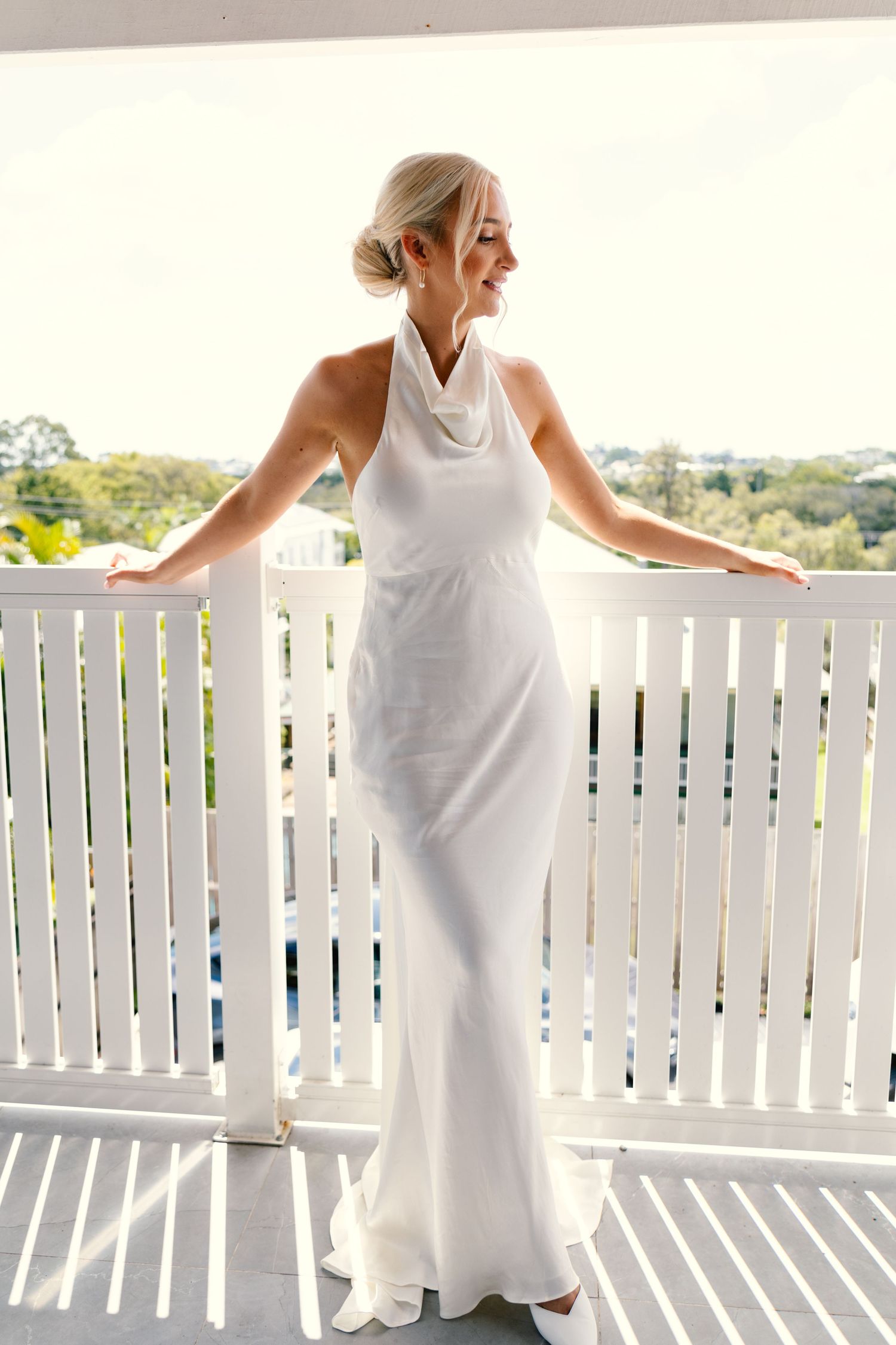 Elegant white halter wedding dress on a bright porch with white railings and scenic background.