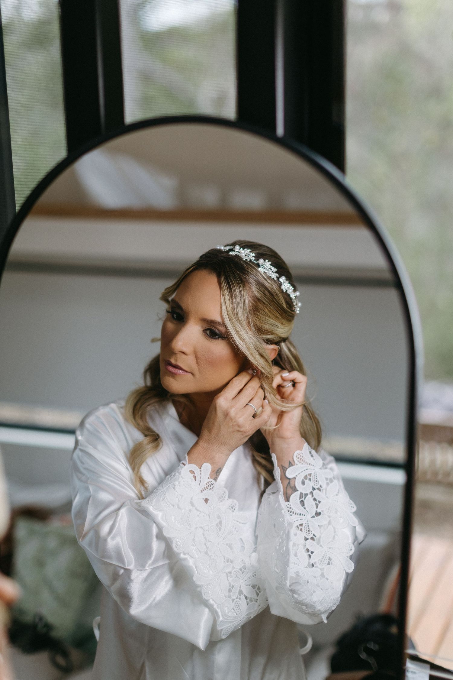 Bride in elegant lace robe preparing for wedding day by mirror.