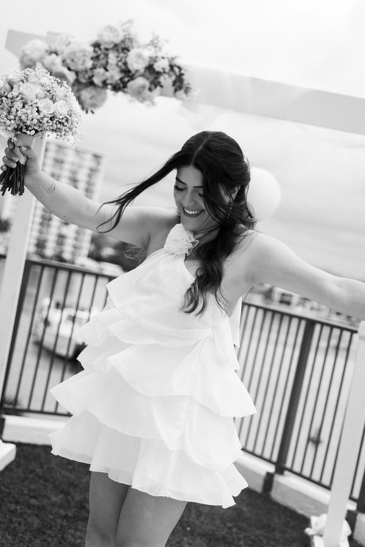 A bride in a flowing white dress twirls joyfully on a porch in black and white photography.