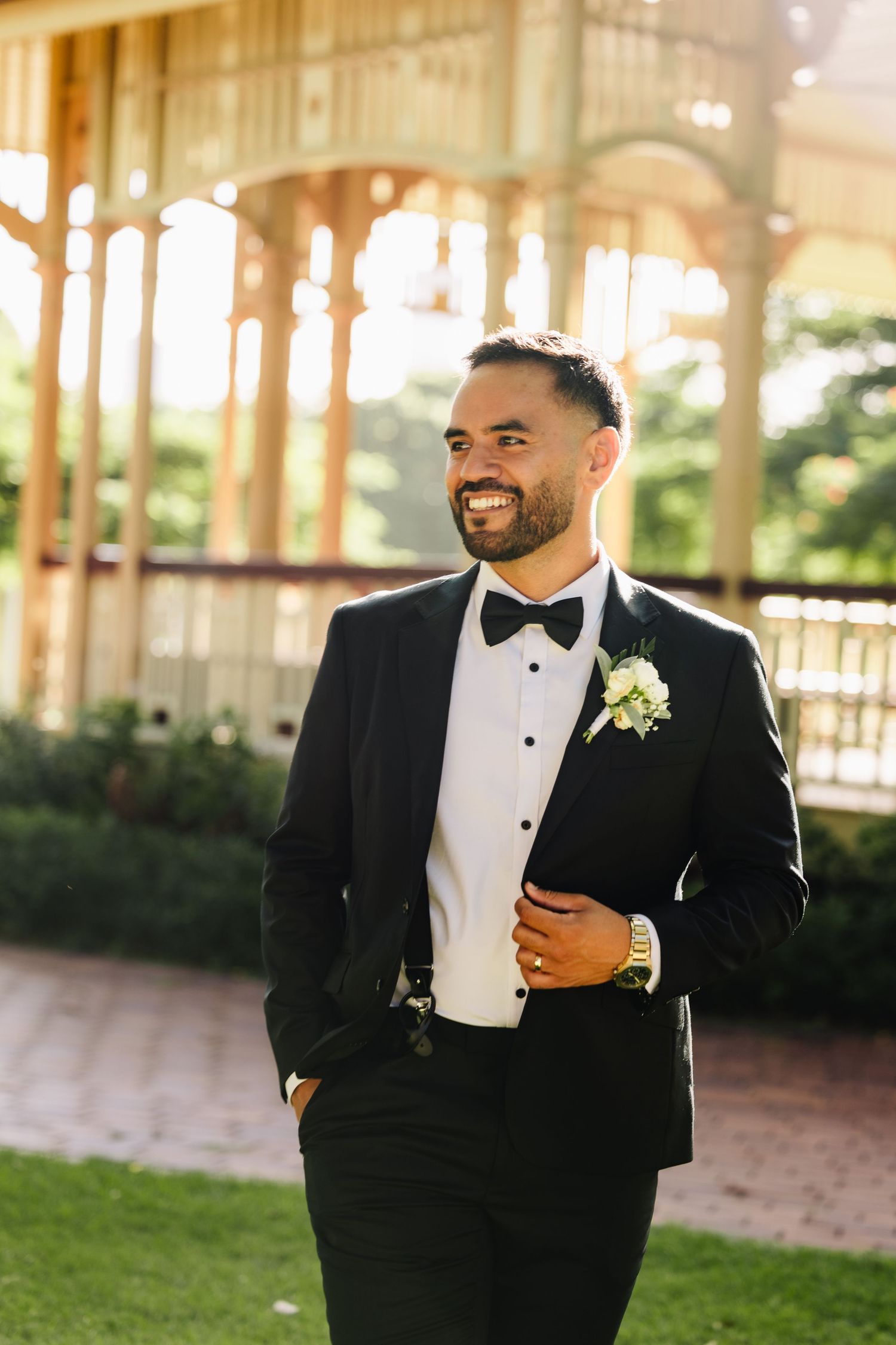 Groomsmen in classic black tuxedos and bow ties pose outdoors at an elegant wedding venue.