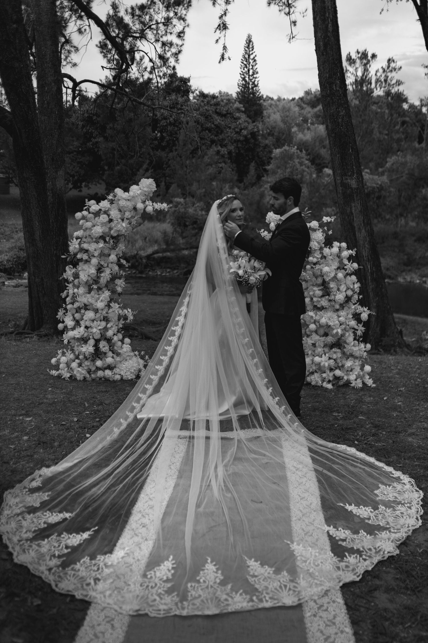An elegant wedding dress with a long lace veil spread out against a natural outdoor backdrop.