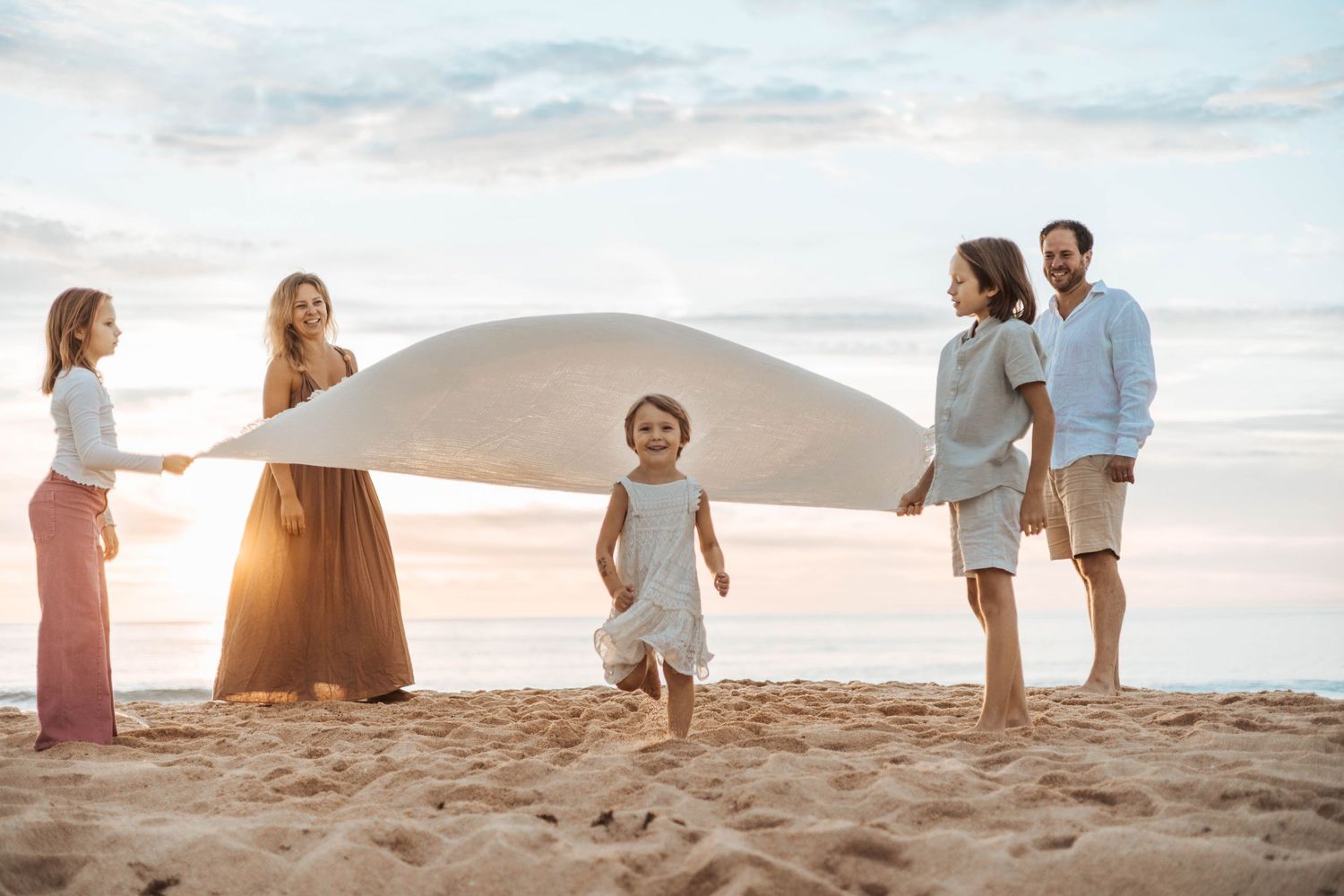 Familj på stranden med ett barn som springer under en filt.