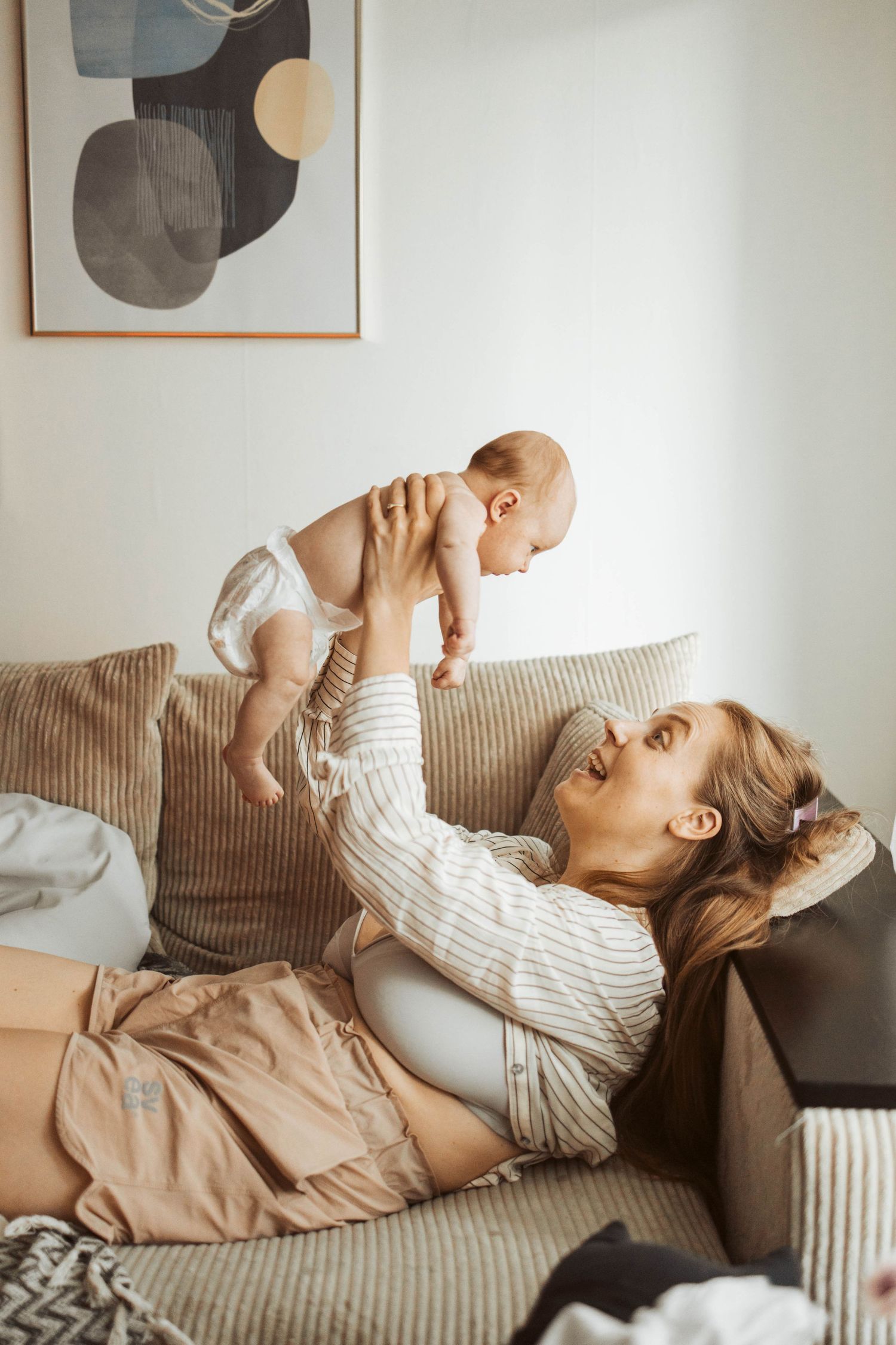 Mamma håller upp nyfödd bebis i soffan.