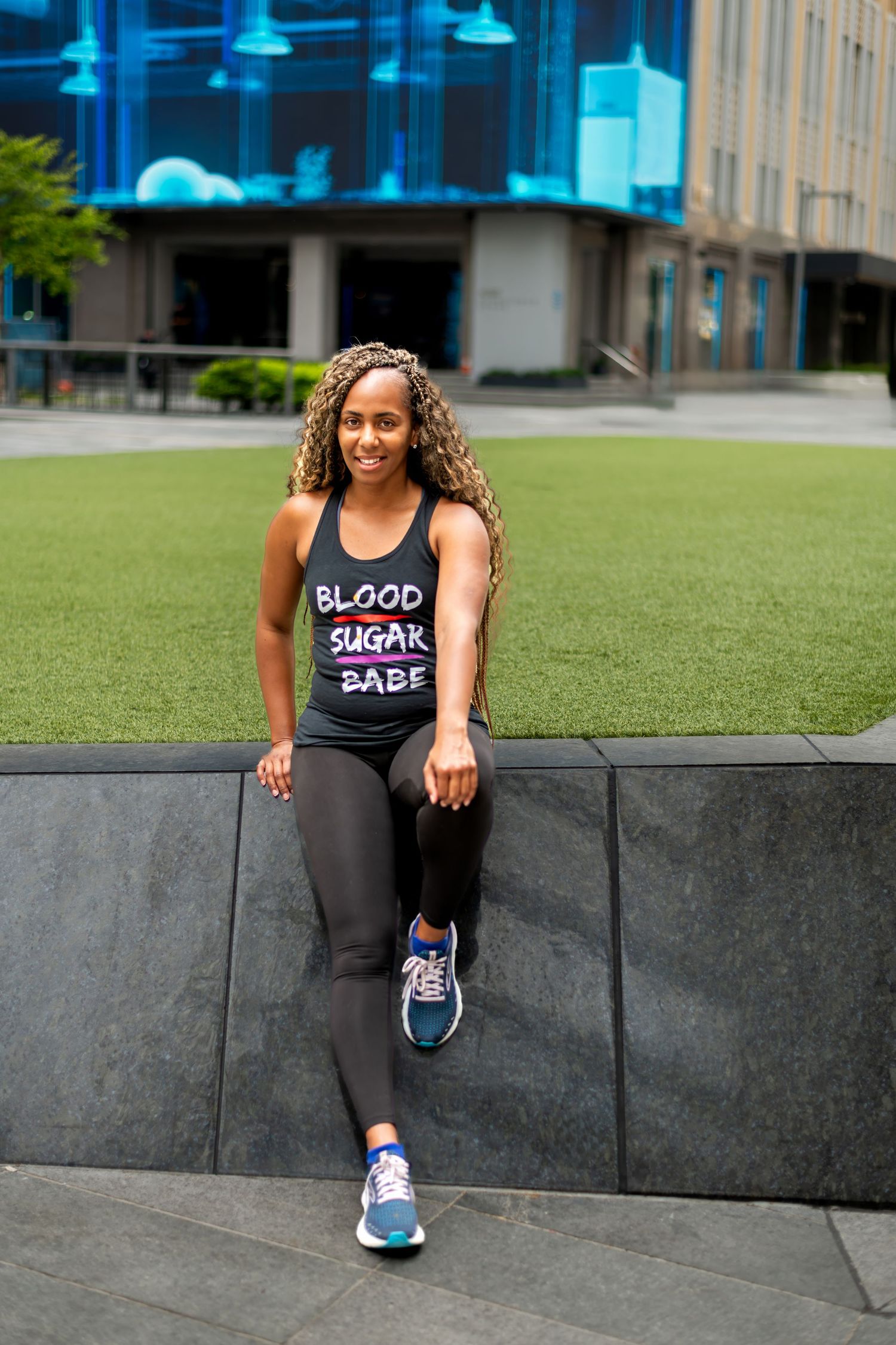 Athletic woman sitting on concrete ledge wearing black workout tank top.