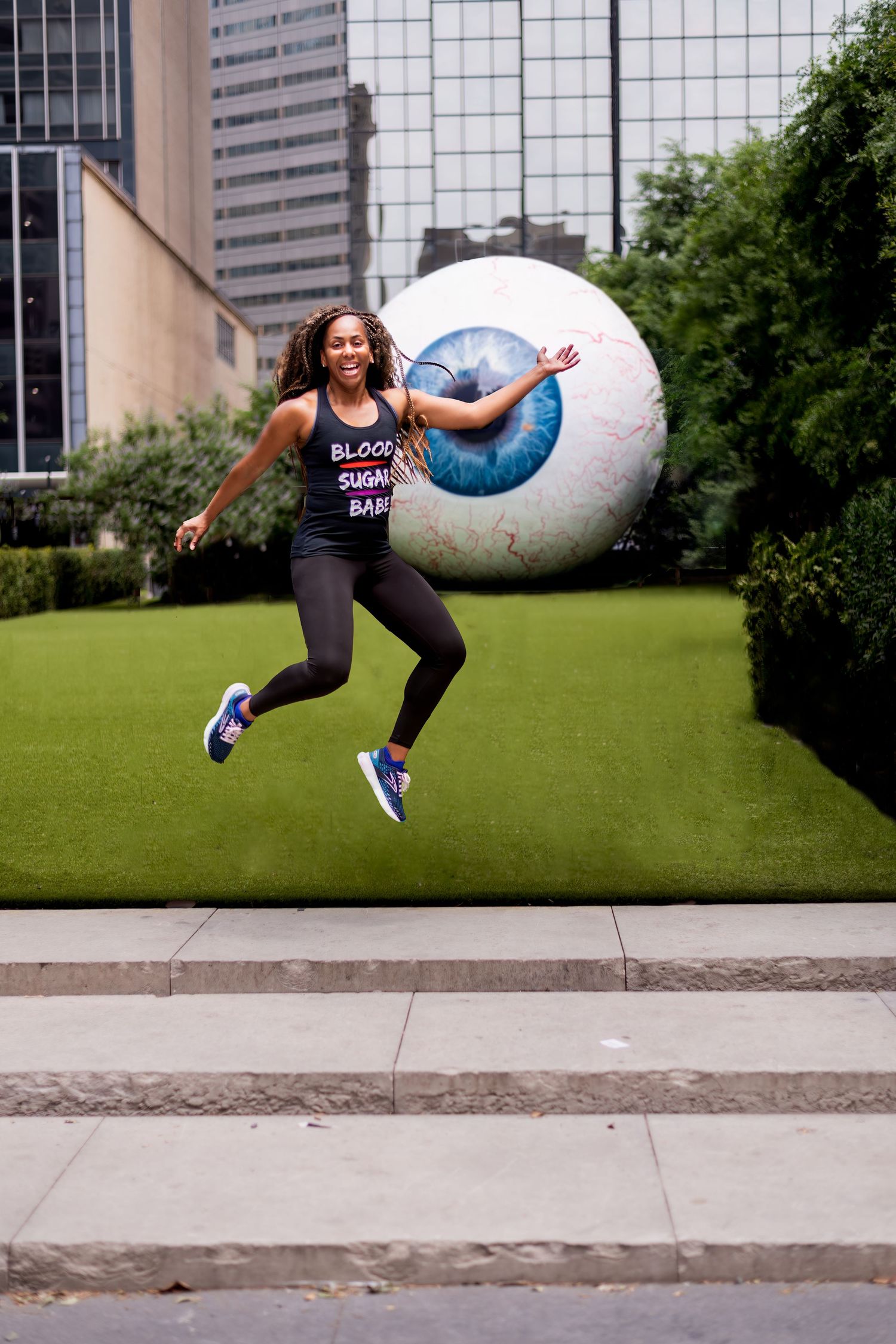 Woman leaping playfully in front of large sculptural eyeball in urban setting.