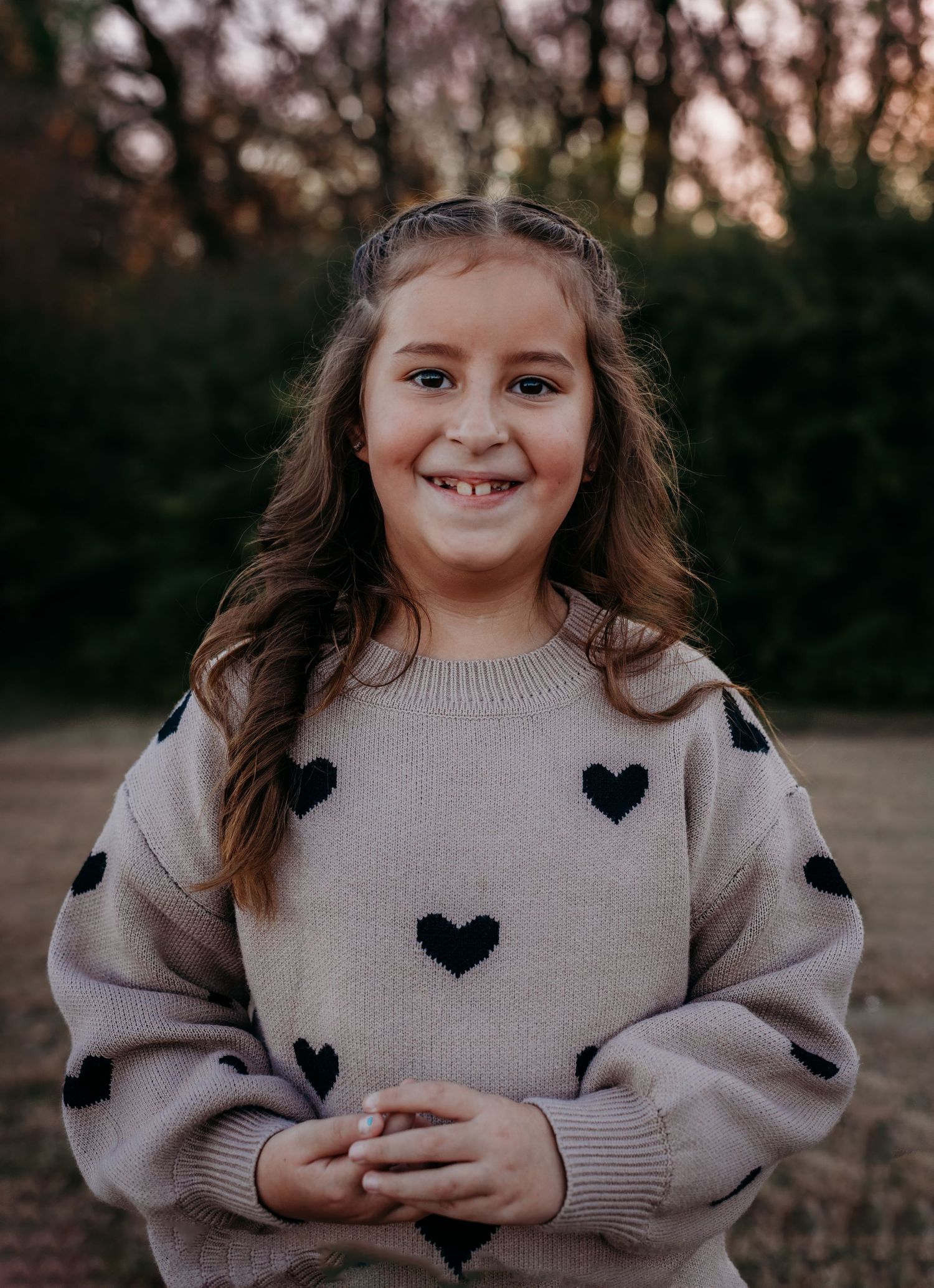 Child wearing sweater with heart pattern smiling during golden hour photoshoot.