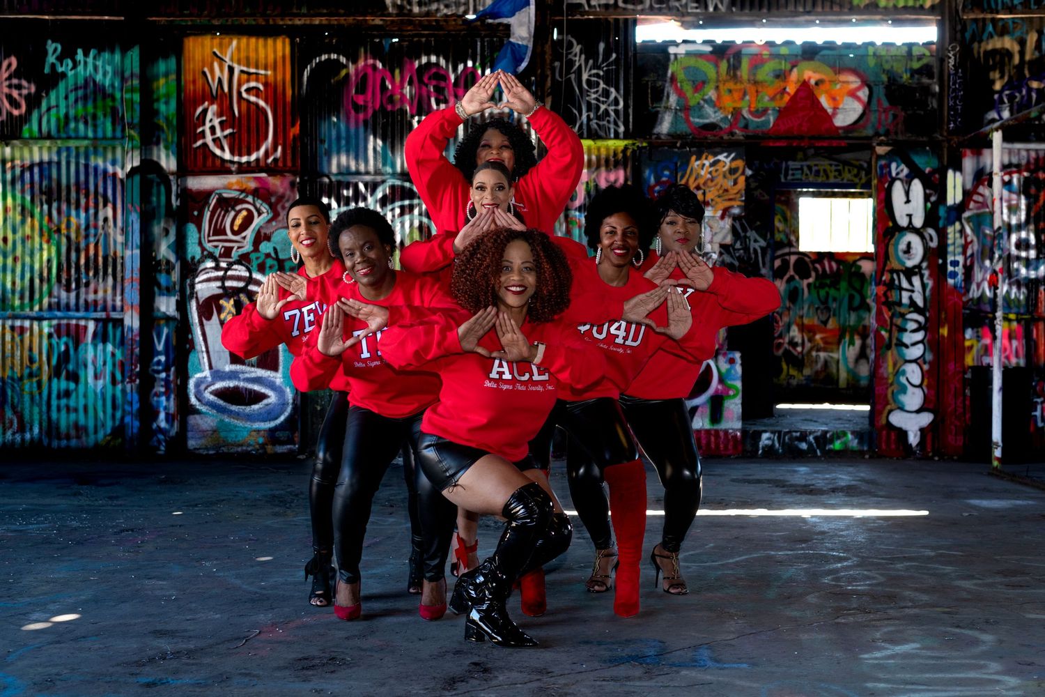 Group of dancers performing in red outfits against colorful graffiti wall backdrop.