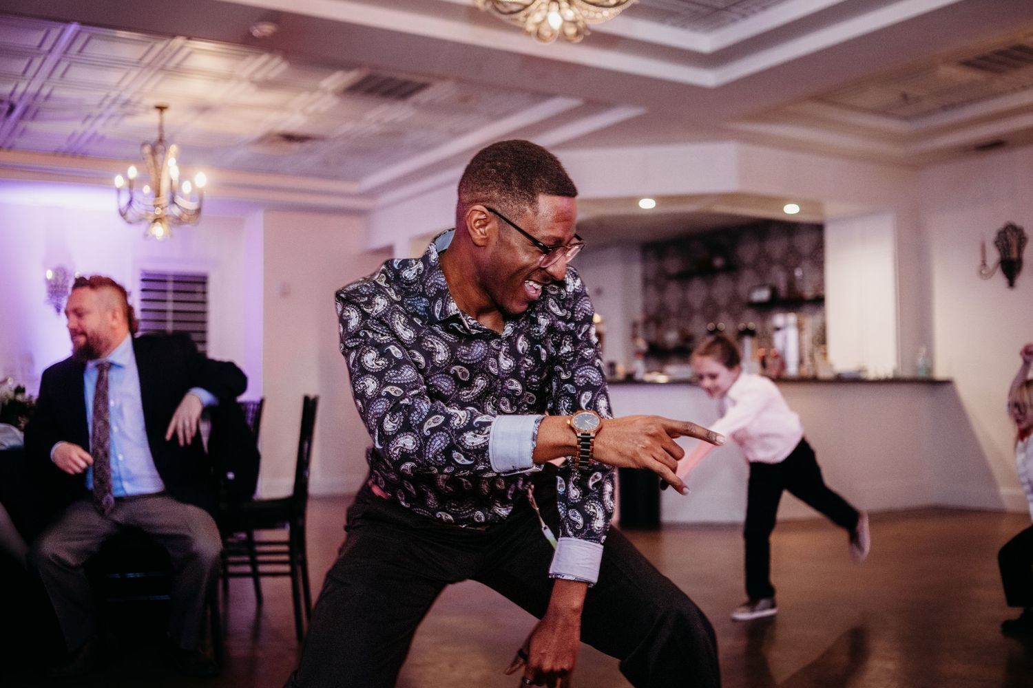 Wedding guests dancing energetically in a ballroom with purple mood lighting.