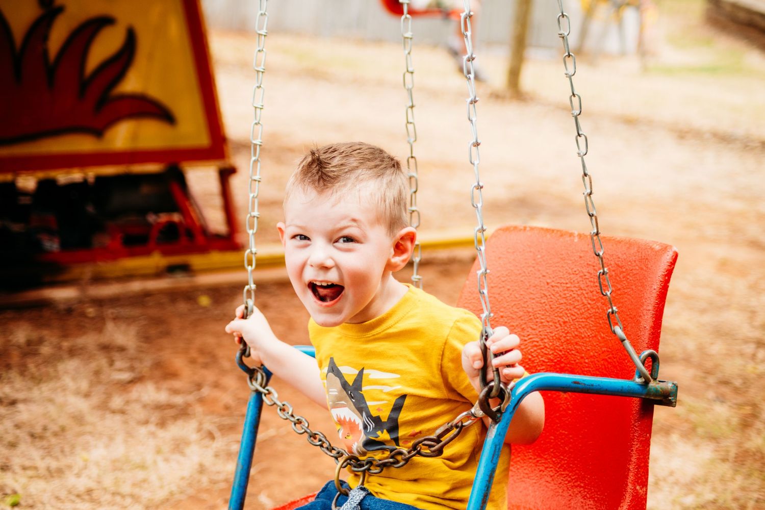 Child swinging happily on playground equipment in bright yellow shirt.