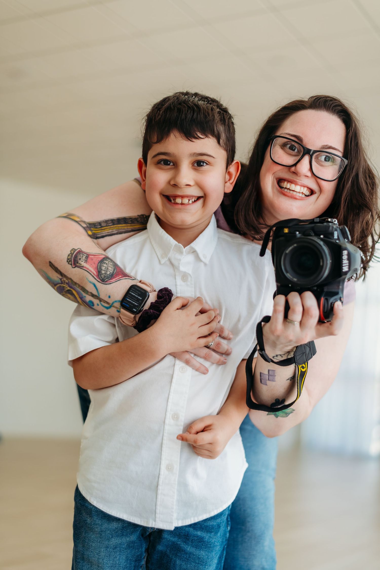 A photographer and young boy pose together holding cameras and smiling in a studio setting.