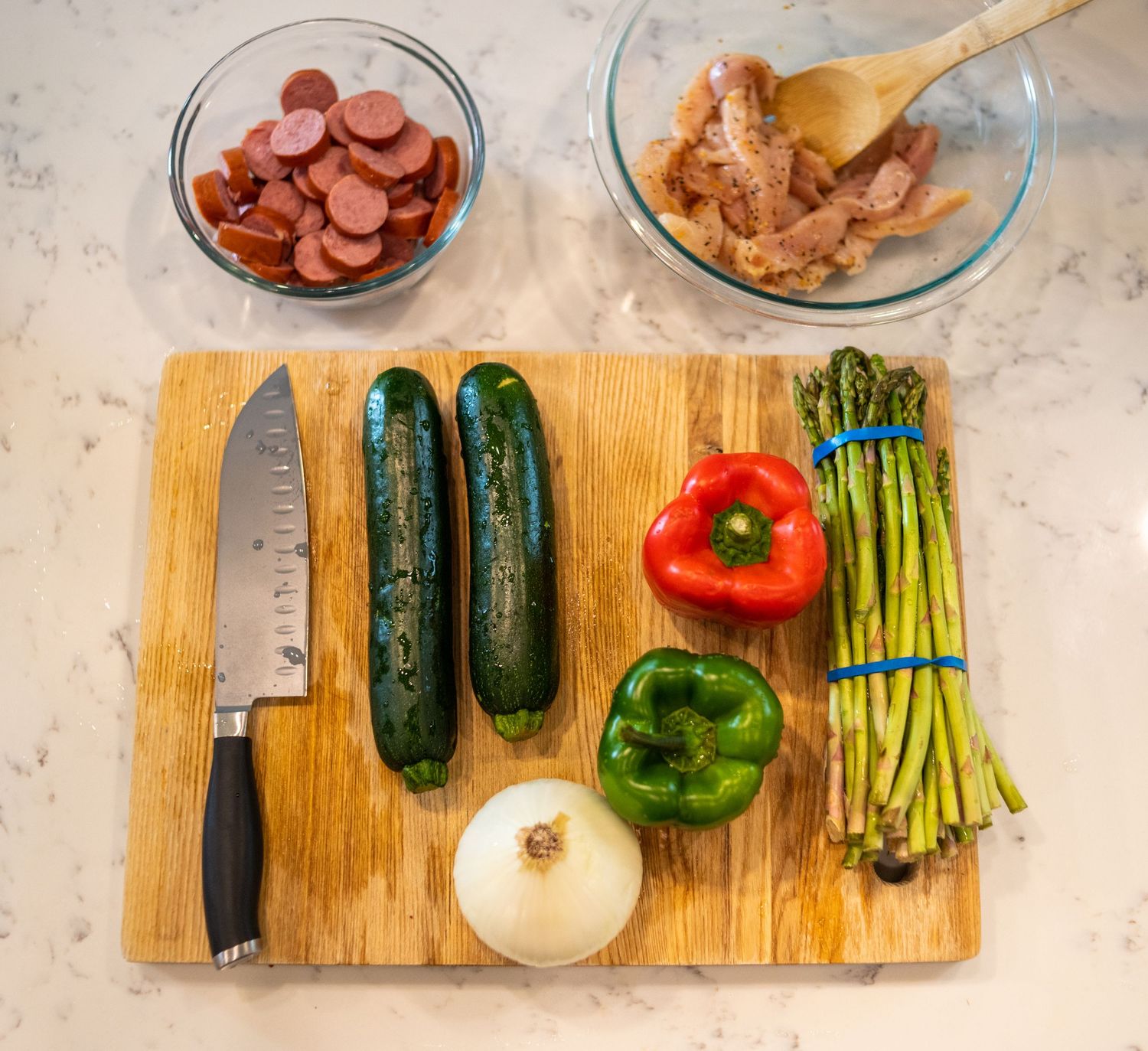 Fresh vegetables including cucumbers, peppers, and asparagus arranged on wooden cutting board.