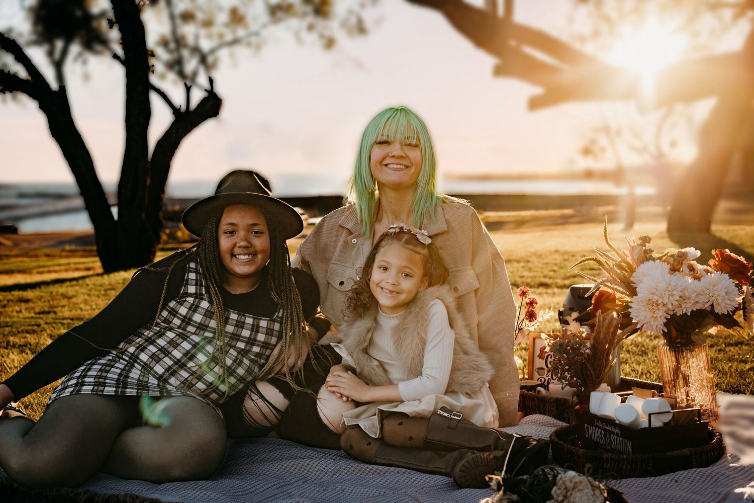 Family enjoying sunset together on blanket under tree with golden light.