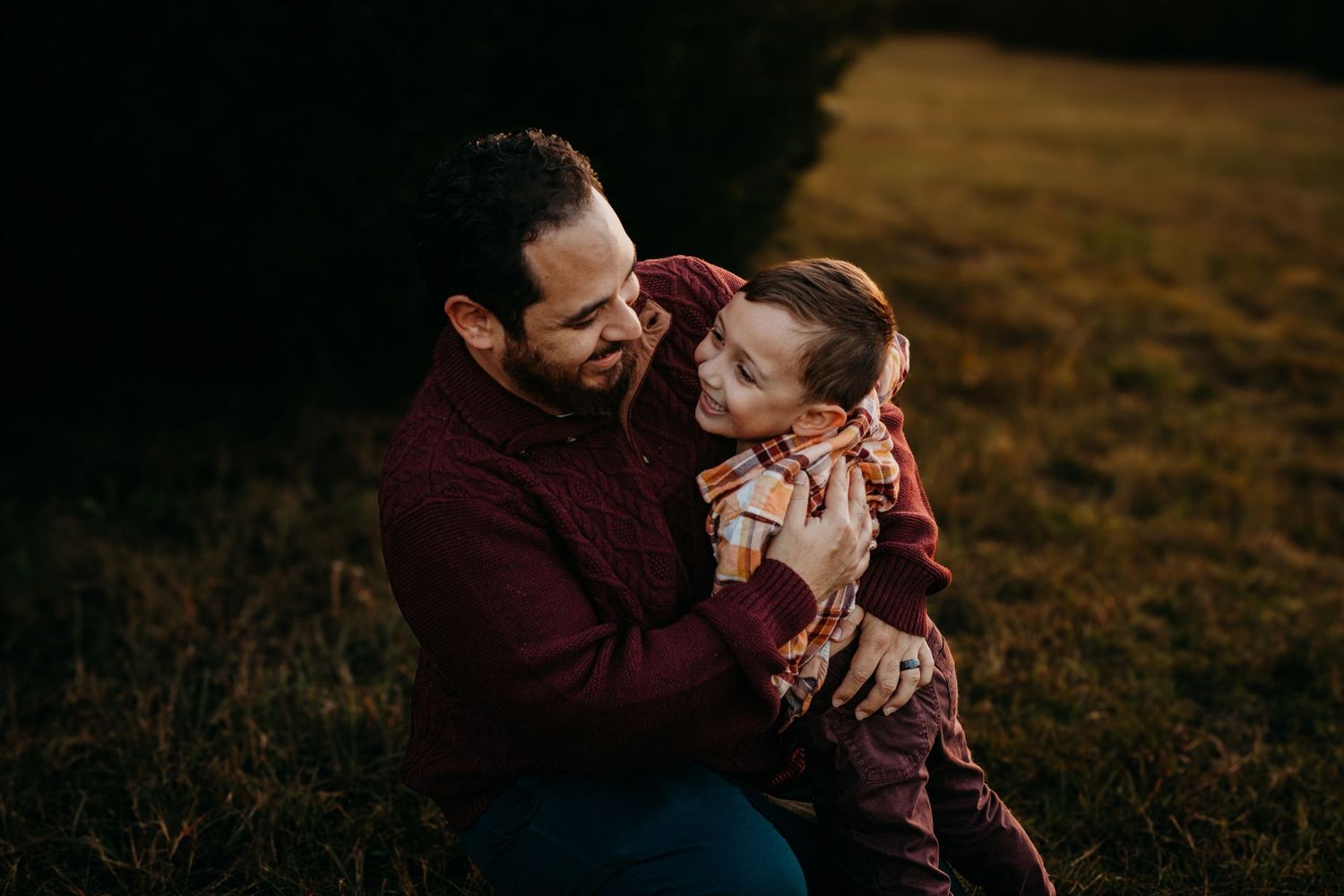 A couple shares tender moments in a golden field at sunset wearing burgundy and white outfits.