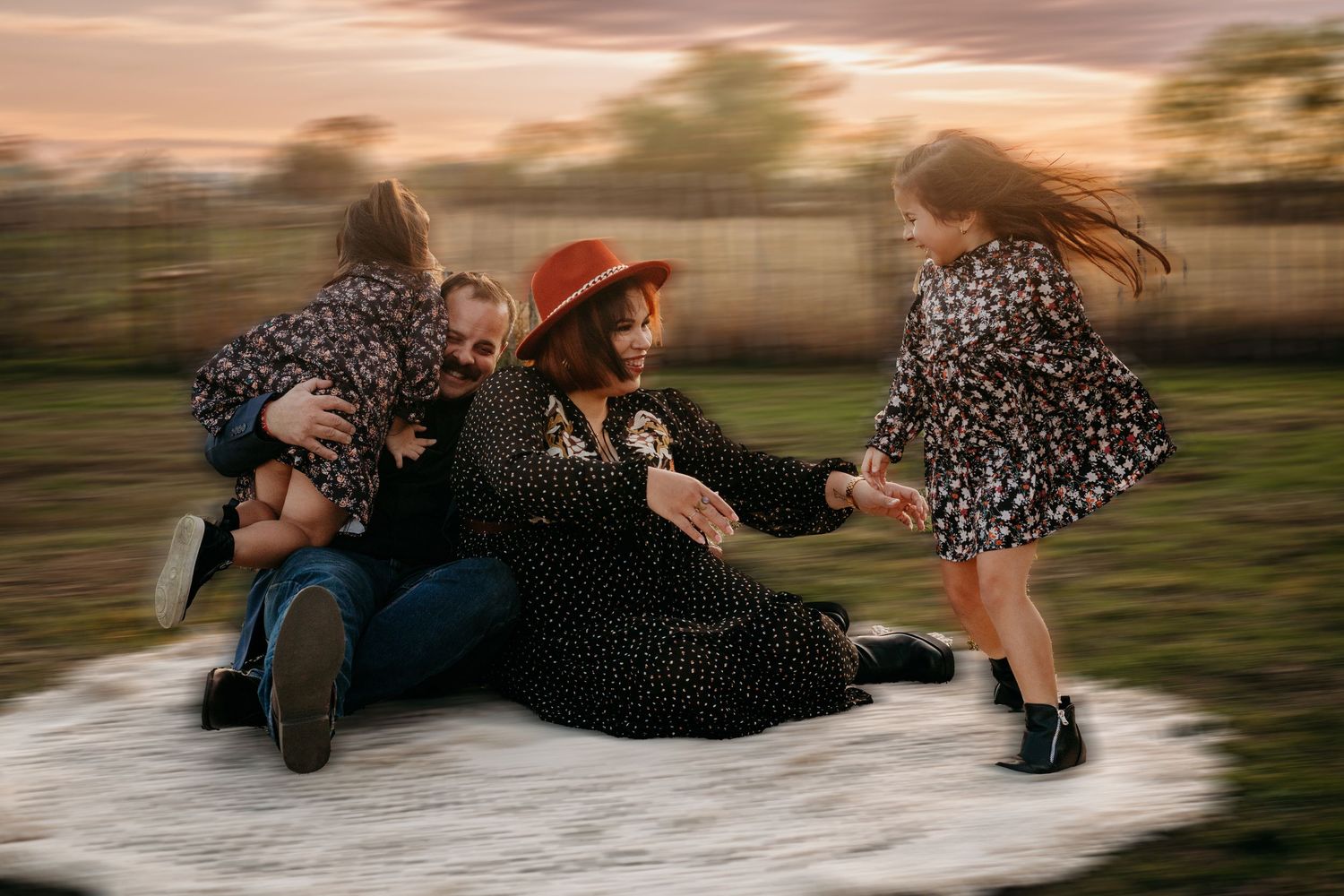 Family members laying on blanket during sunset photoshoot in field.