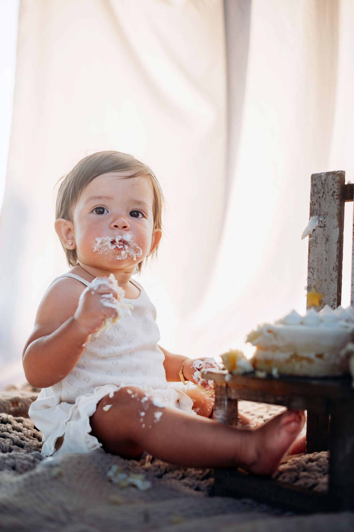 A messy cake smash photo featuring a baby covered in frosting with a white backdrop.