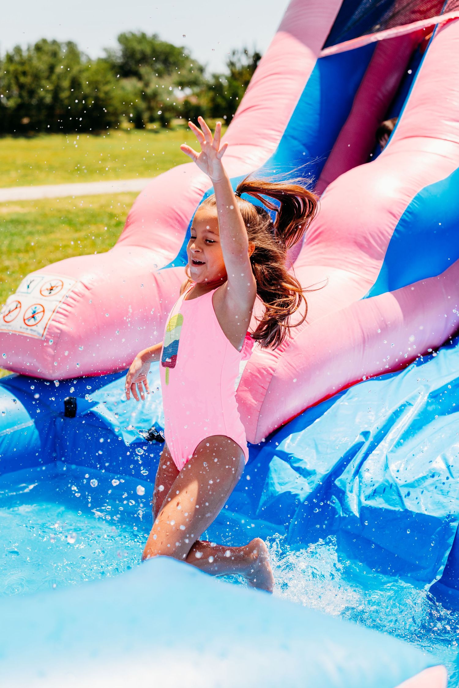 People splashing down a pink and blue inflatable water slide on a sunny summer day.