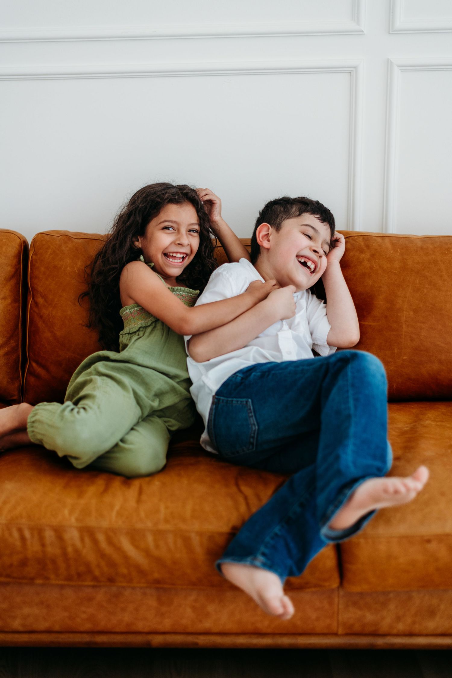 Playful moment captured on brown leather couch showing genuine laughter and joy.