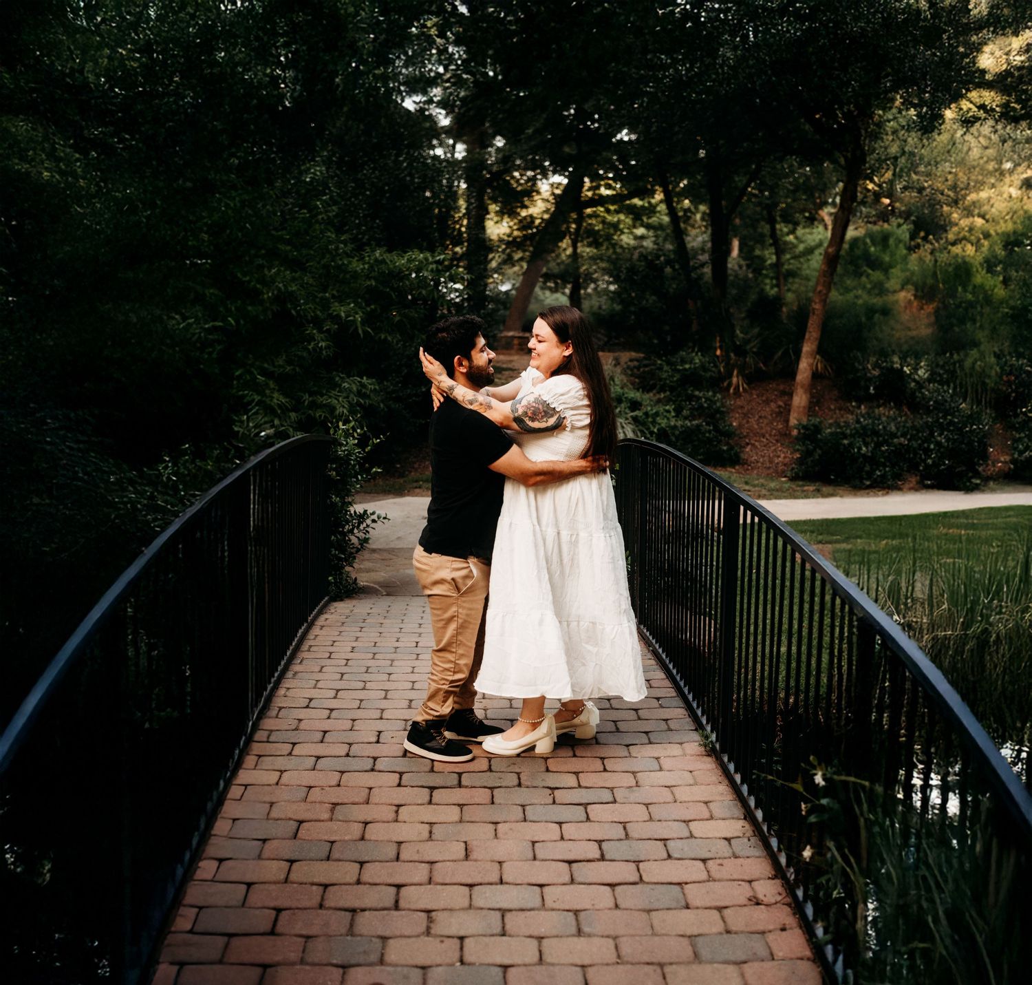 Couple dancing together on a brick pathway surrounded by garden railings at dusk.