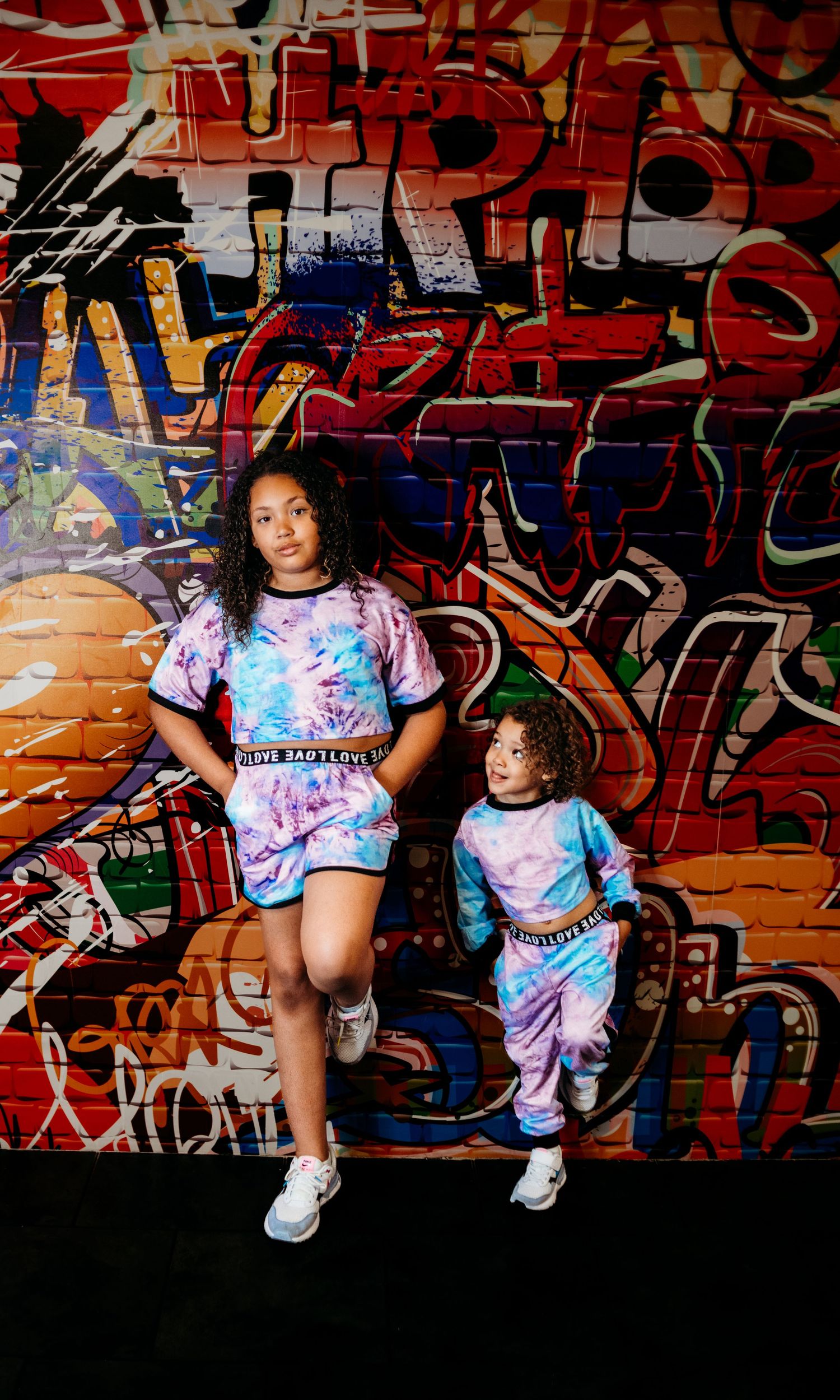 Urban photoshoot with tie-dye outfits against colorful graffiti wall background.