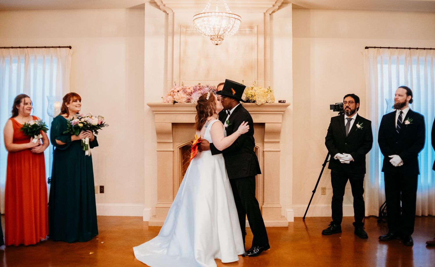 Wedding guests celebrate in a bright ballroom with elegant chandeliers and white decor.