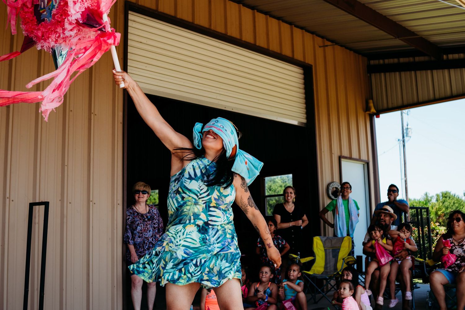 A performer in a turquoise dress and wig dances energetically on stage at an outdoor venue while holding a pink prop.