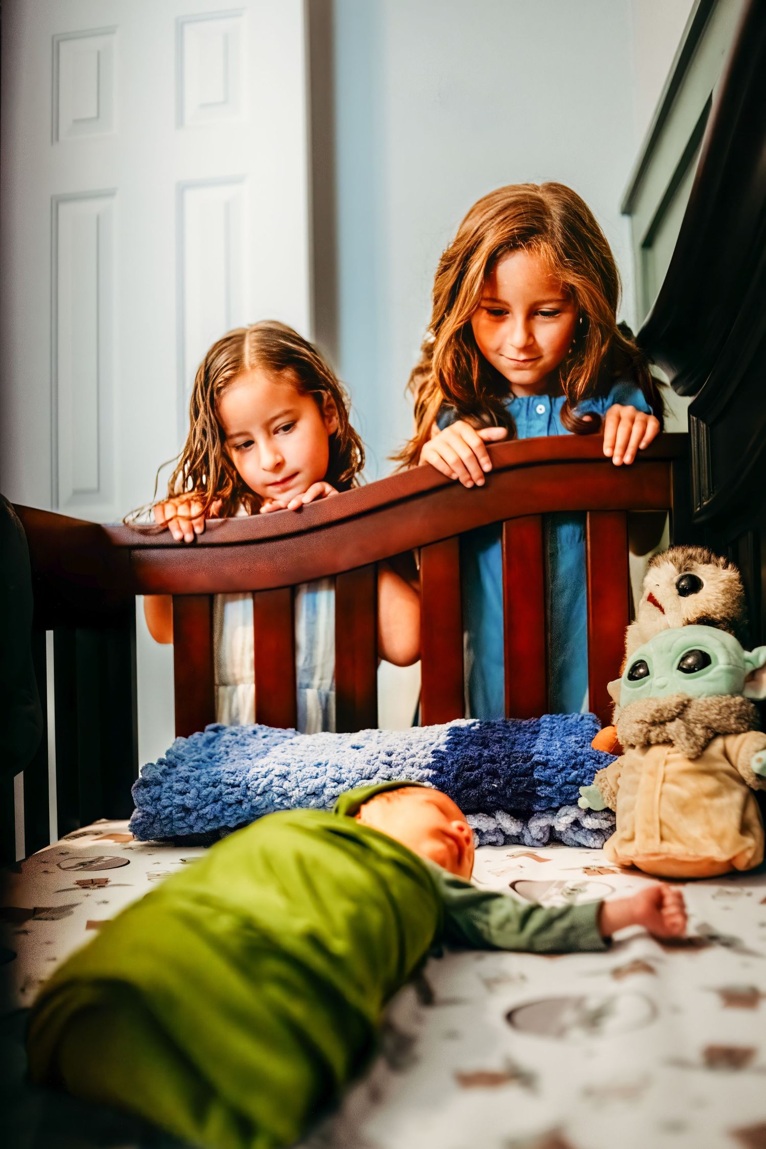 Two children peek over a wooden banister with stuffed toys nearby.