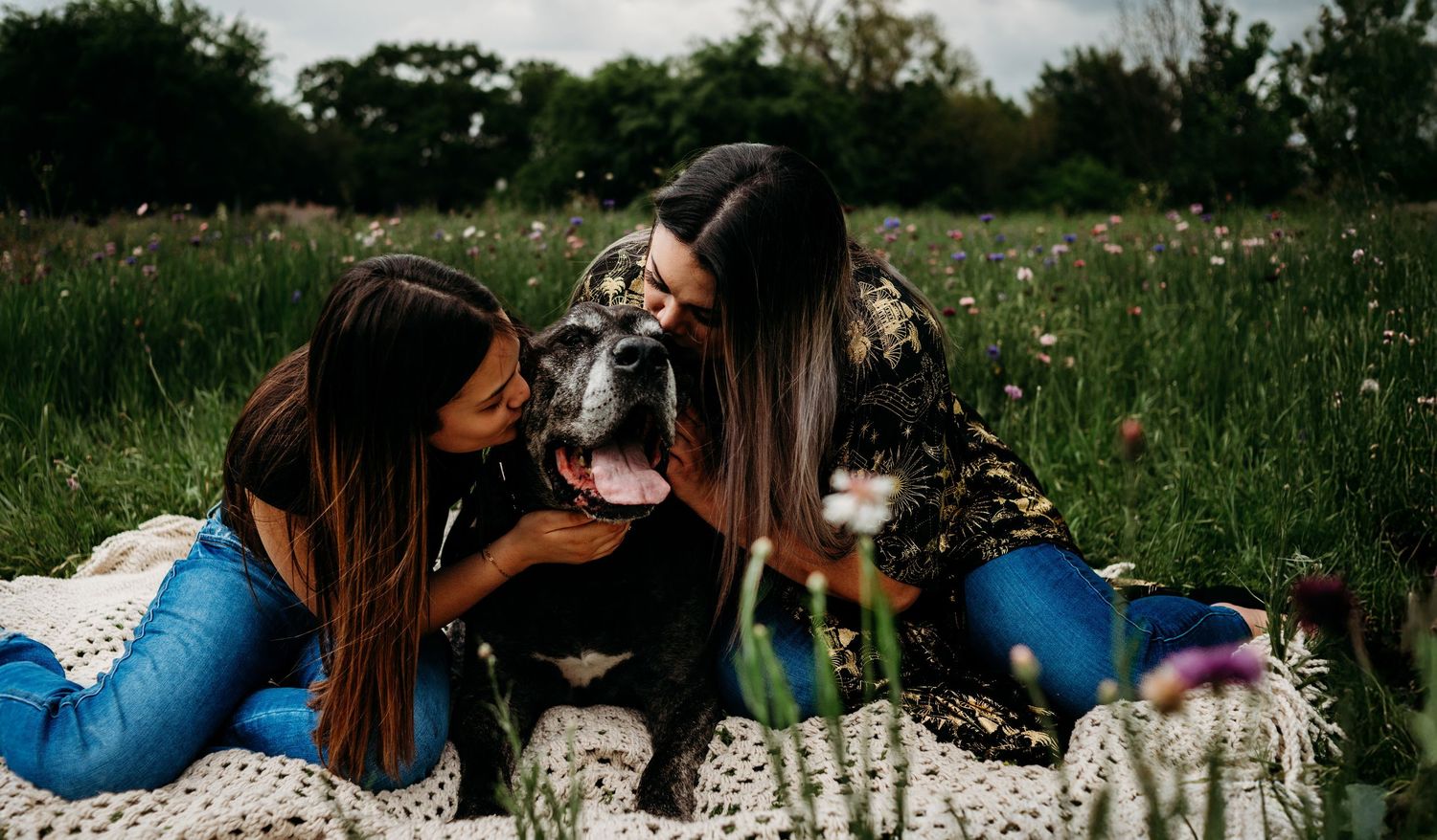 Friends lounging on blanket with pets in blooming spring meadow.