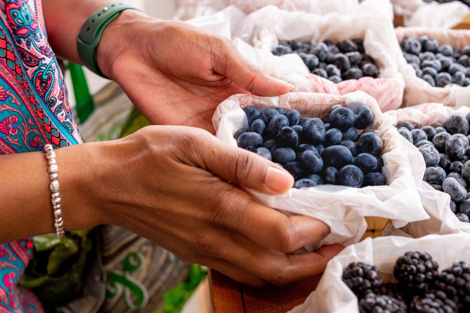 Fresh blueberries and blackberries being sorted by hands on a white surface.