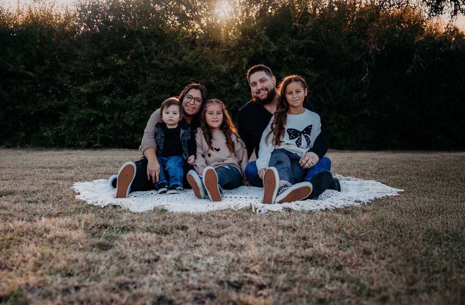 Group relaxing on blanket in grassy field during sunset photo session.